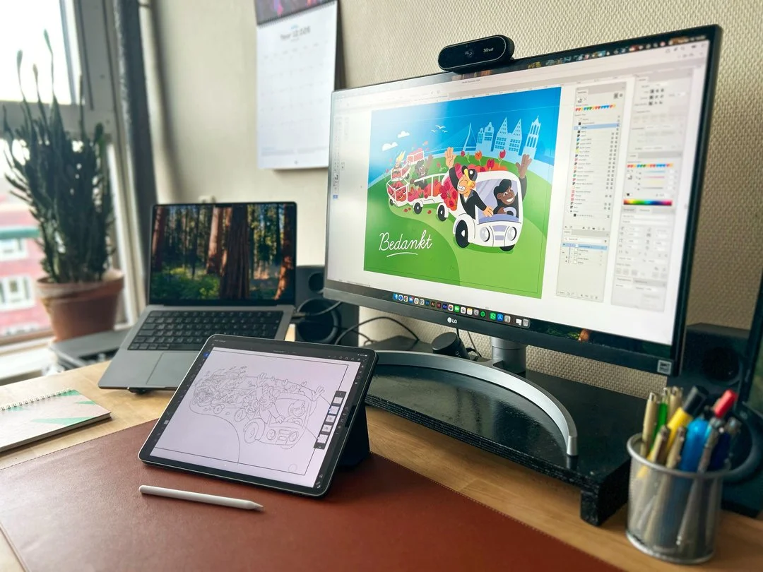 Een werkplek met een monitor die een kleurrijke wenskaart toont en een iPad als tekentablet waar de schets van de wenskaart op te zien is.