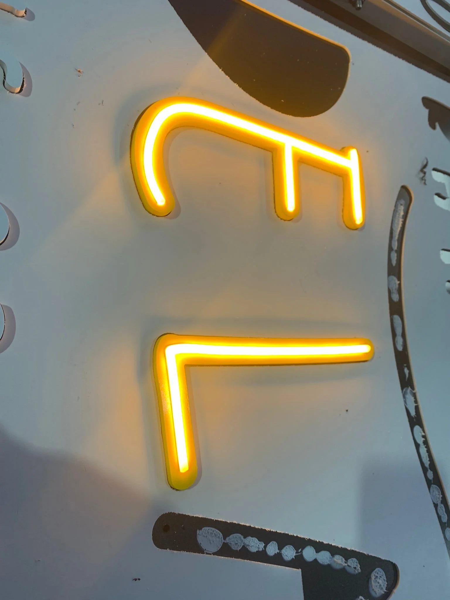 Letras en neón amarillo formando la palabra 'ON' sobre una superficie blanca con algunas manchas y marcas.