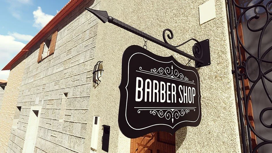 Cartel que dice 'Barber Shop' colgado en la pared de un edificio con detalles decorativos en blanco y negro.