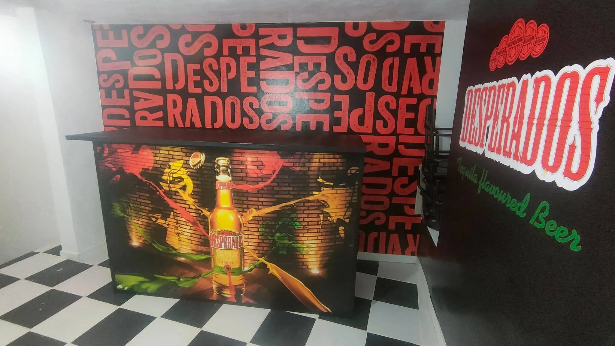 Cartel promocional de una marca de cerveza con fondo de ladrillos, botella de cerveza con líquido dorado, y llamativos efectos de explosión en naranja y rojo.