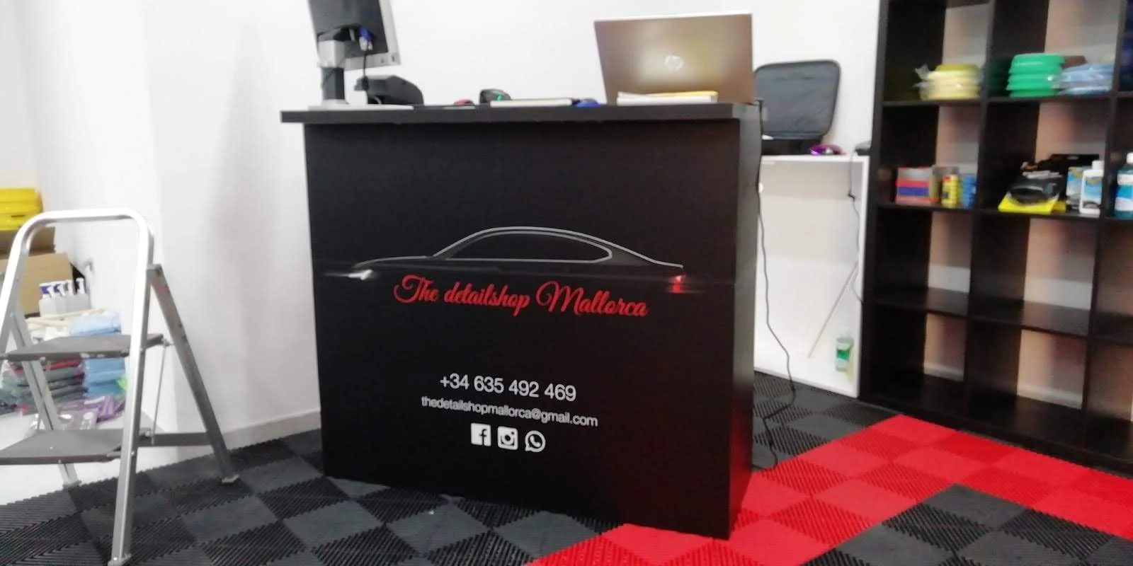 Mostrador de tienda de detalles con contacto y redes sociales en Mallorca, en una oficina con estanterías y sillas.