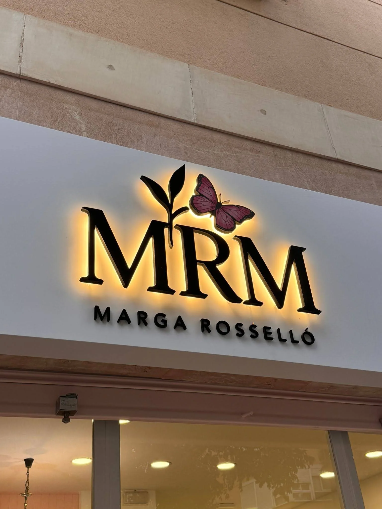 Cartel iluminado con letras negras y una mariposa rosa, que dice 'MIMA' y abajo 'MARGA ROSSELLÓ' en un establecimiento.