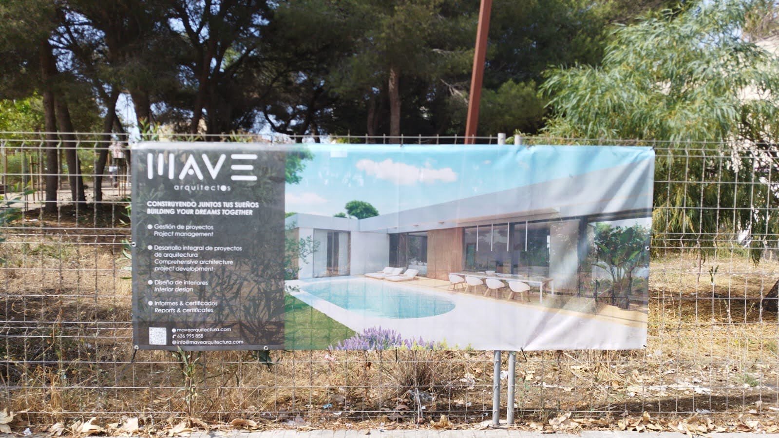 Cartel de construcción de una casa moderna con piscina y áreas de descanso, con árboles y vegetación alrededor.