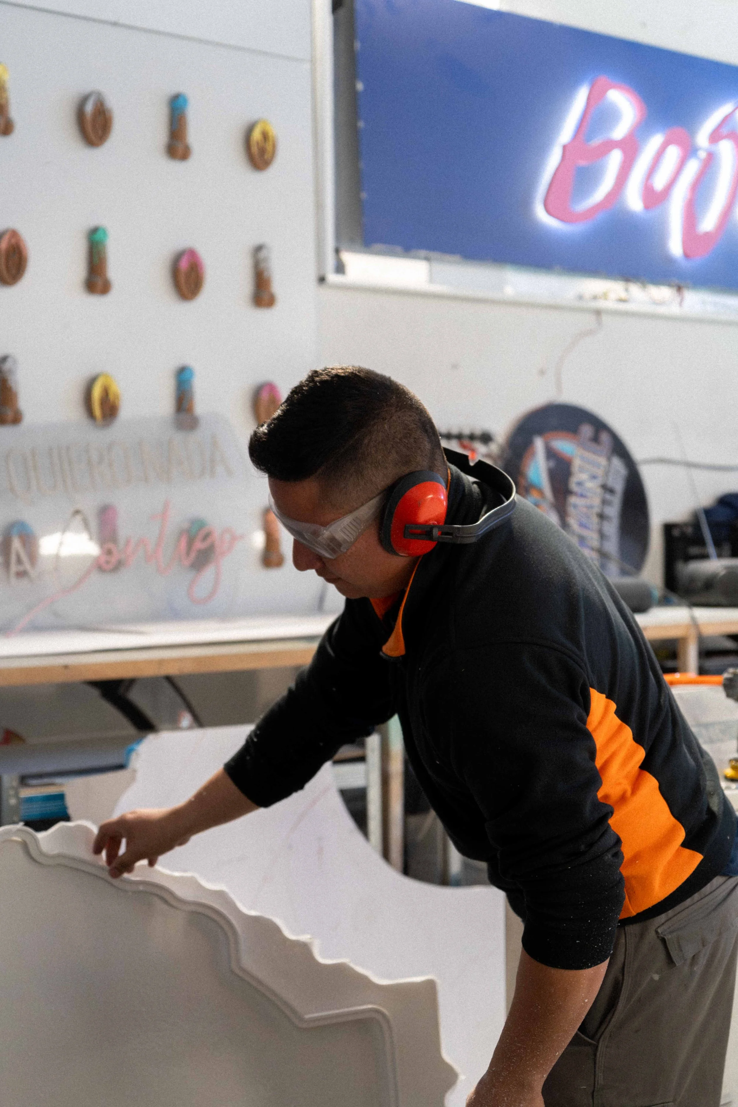 Un joven trabajando en un taller, usando protección auditiva y visual, ajustando o montando una pieza de madera decorativa.