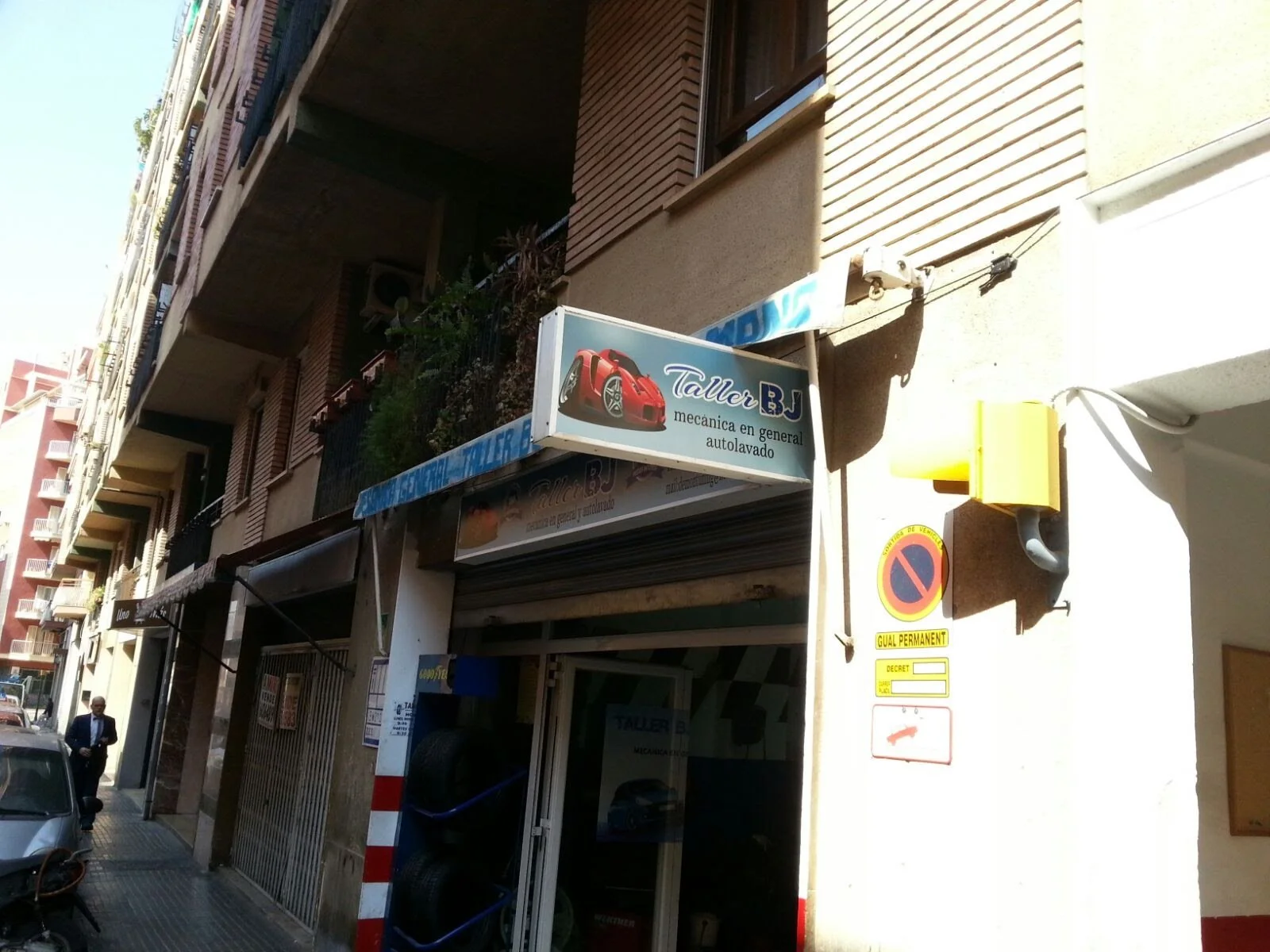 Fachada de un taller mecánico llamado Taller BJ, que ofrece servicios de mecánica en general y autolavado, en un edificio de varias plantas en la ciudad.