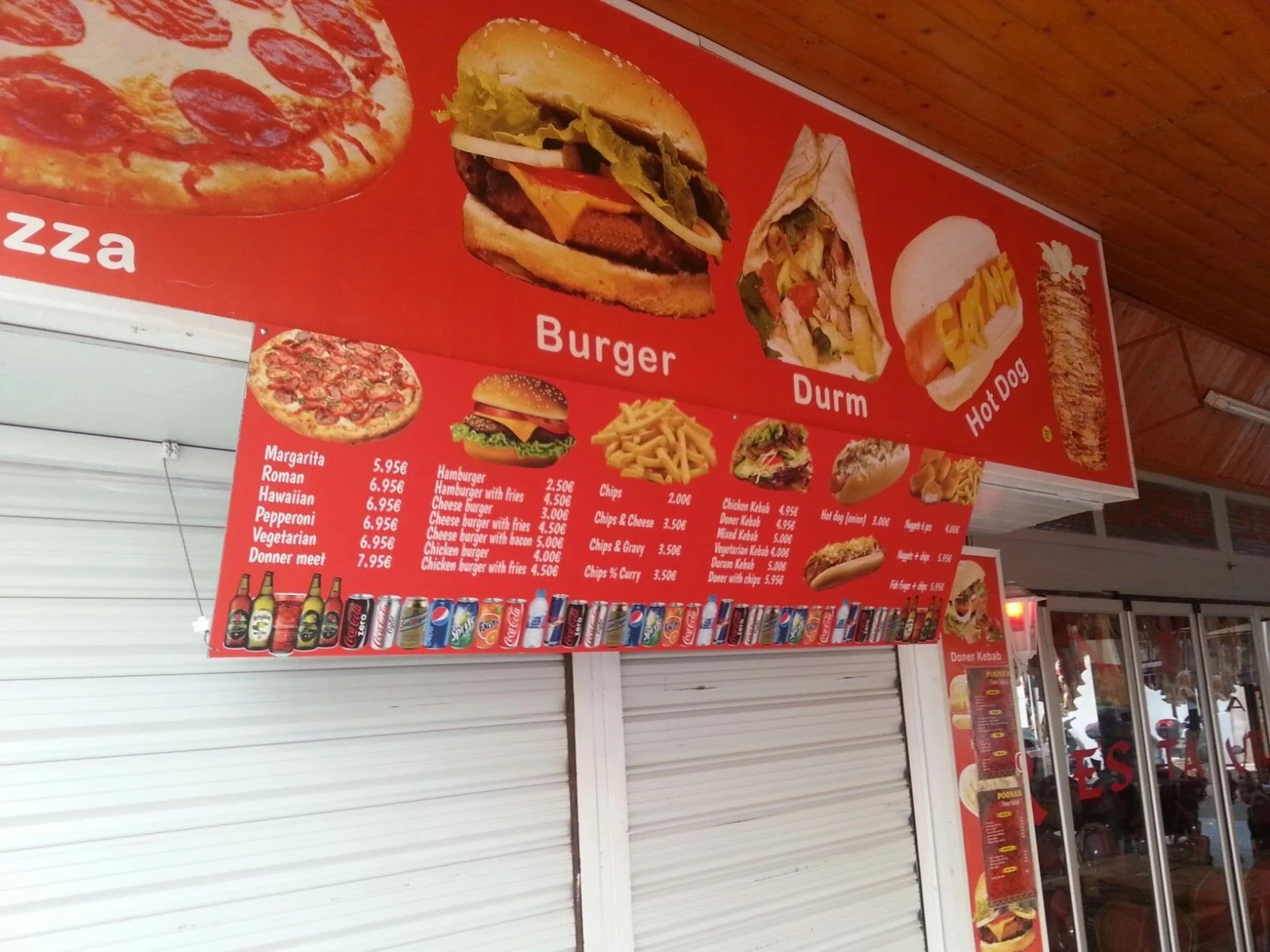 Cartel de menú en un restaurante que ofrece pizzas, hamburguesas, durums, hot dogs y bebidas. Incluye precios y opciones de comida.