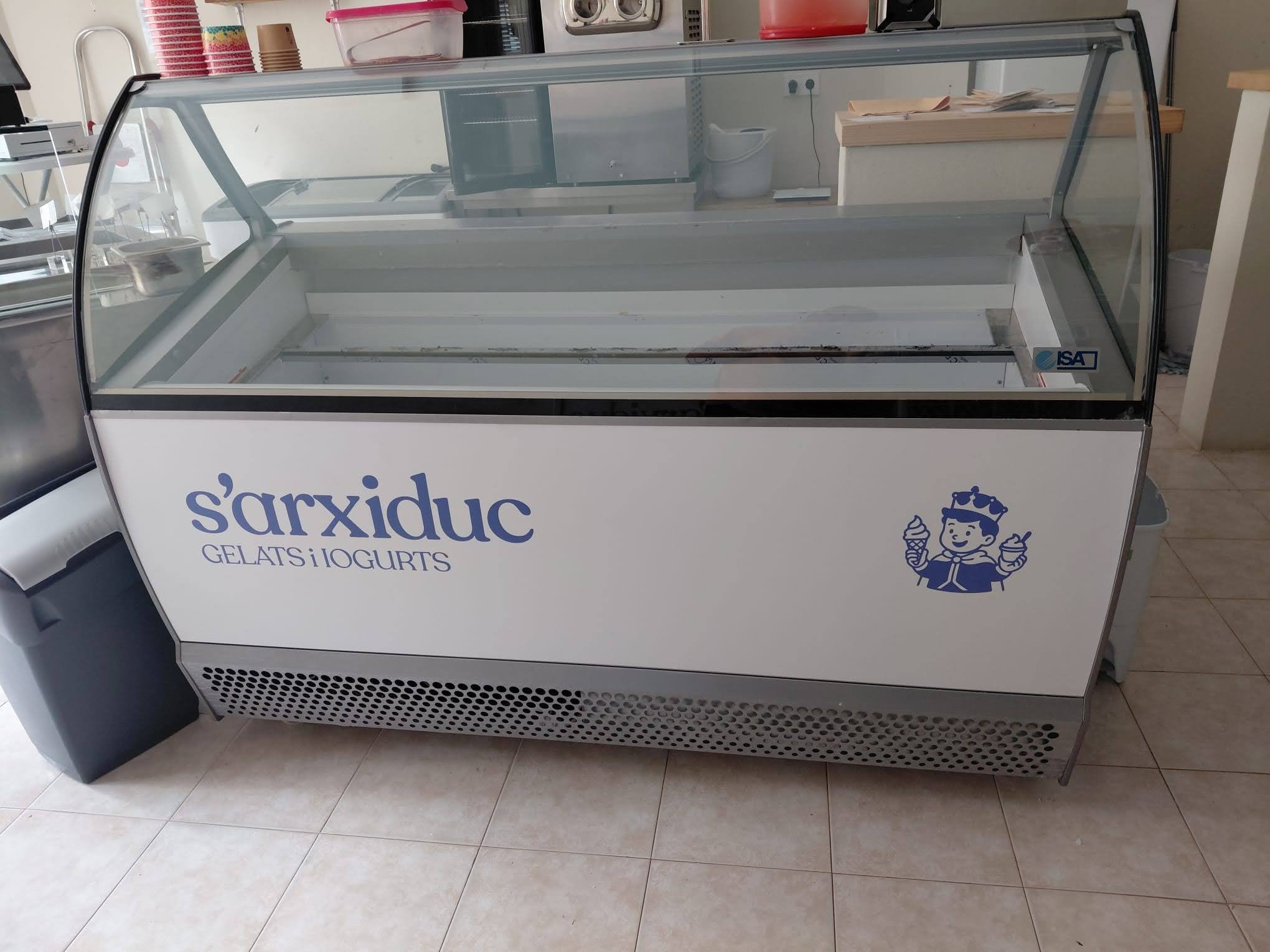 Máquina de helados y yogures con el logotipo de S'arkixduc y una ilustración de un niño con corona sosteniendo un helado en cada mano.