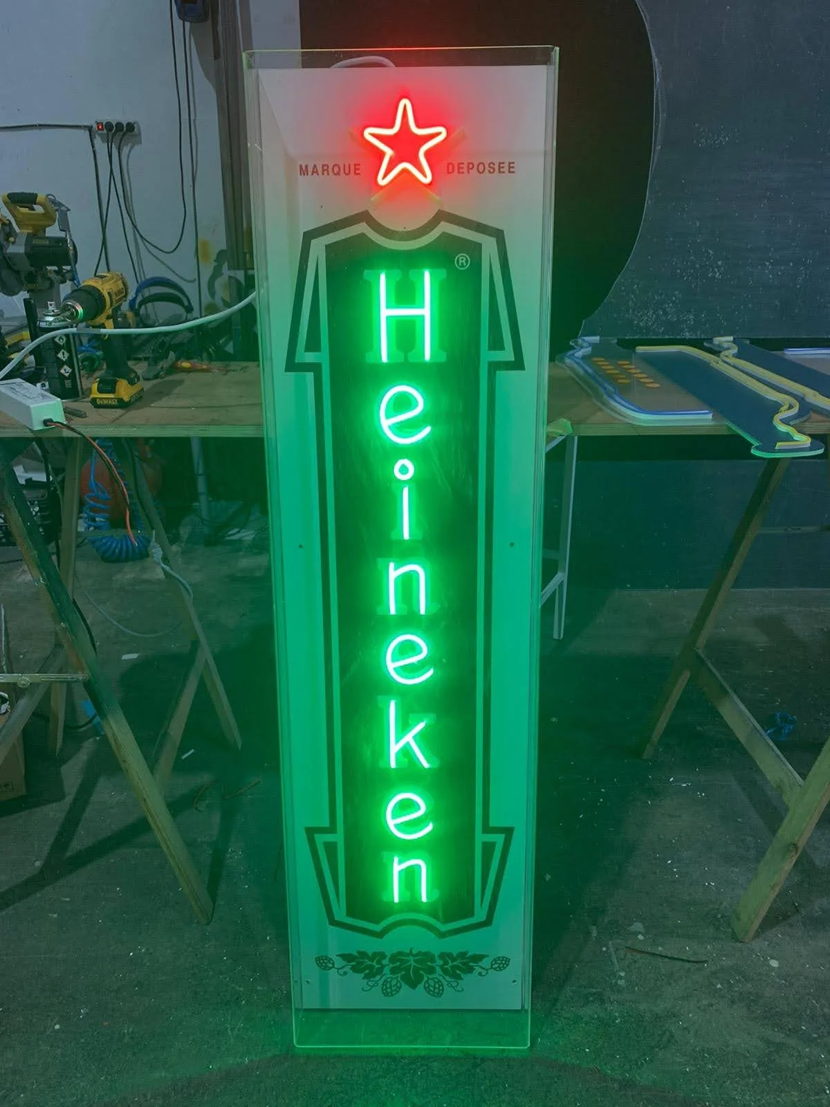 Letrero de neón verde que dice 'Heineken' con un símbolo de estrella roja en la parte superior y un diseño de hojas de lúpulo en la parte inferior