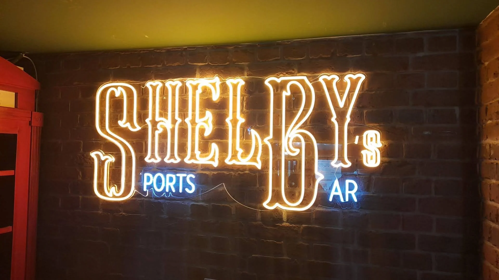 Letrero de neón para un bar llamado 'Sherky's', que indica que sirven 'Wports' y 'Bar' en una pared de ladrillos.