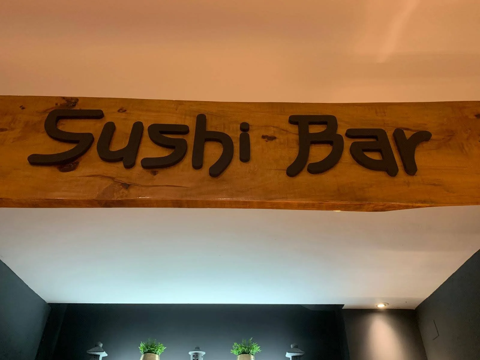 Señal que dice 'Sushi Bar' en letras negras en una pared de madera en el interior de un restaurante.