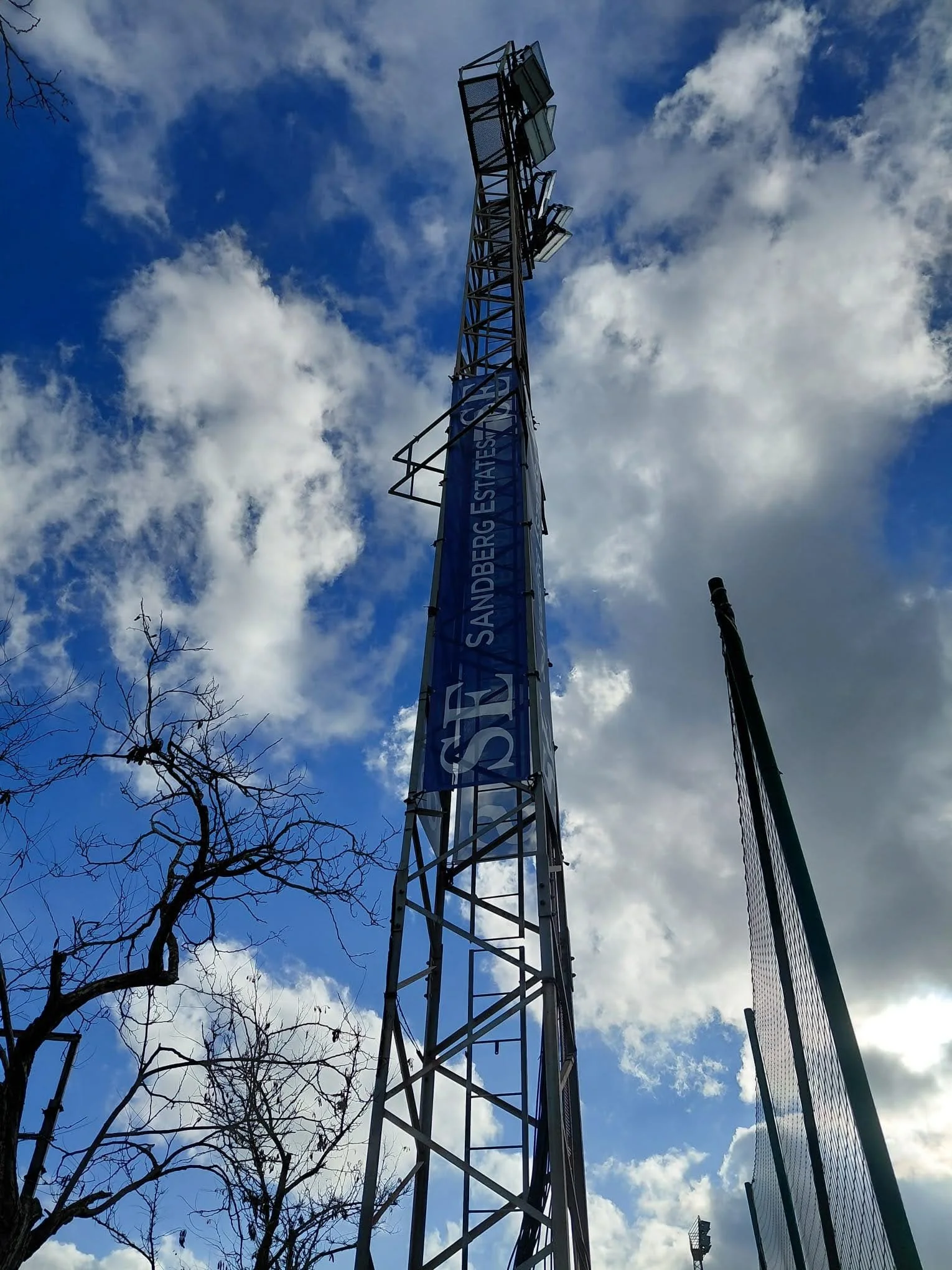 Torres de transmisión eléctrica en un día soleado con cielo parcialmente nublado y árboles en primer plano.