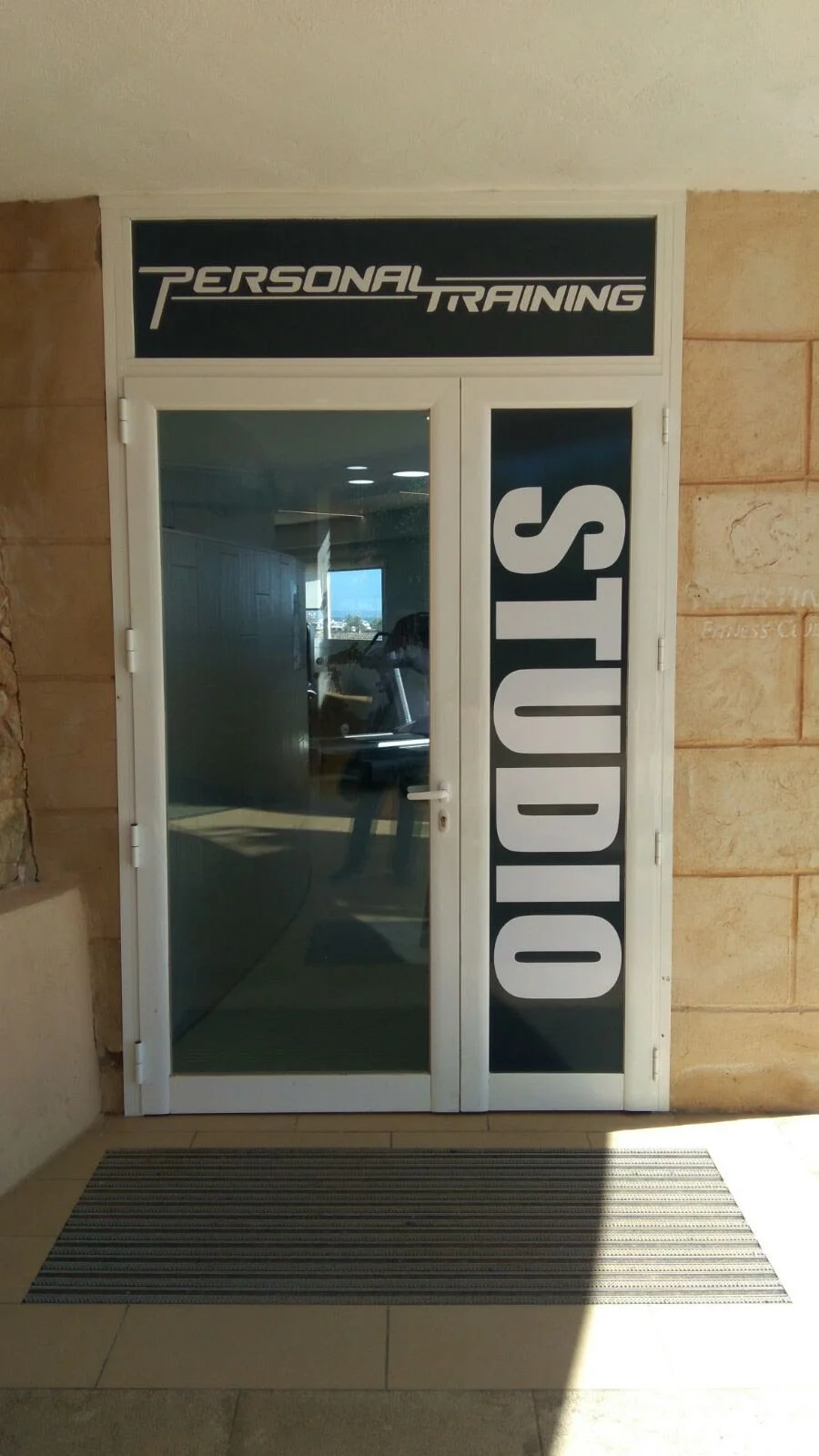Puerta de un gimnasio con letrero que dice 'Personal Training' en la parte superior y 'Studio' en una franja vertical al lado.