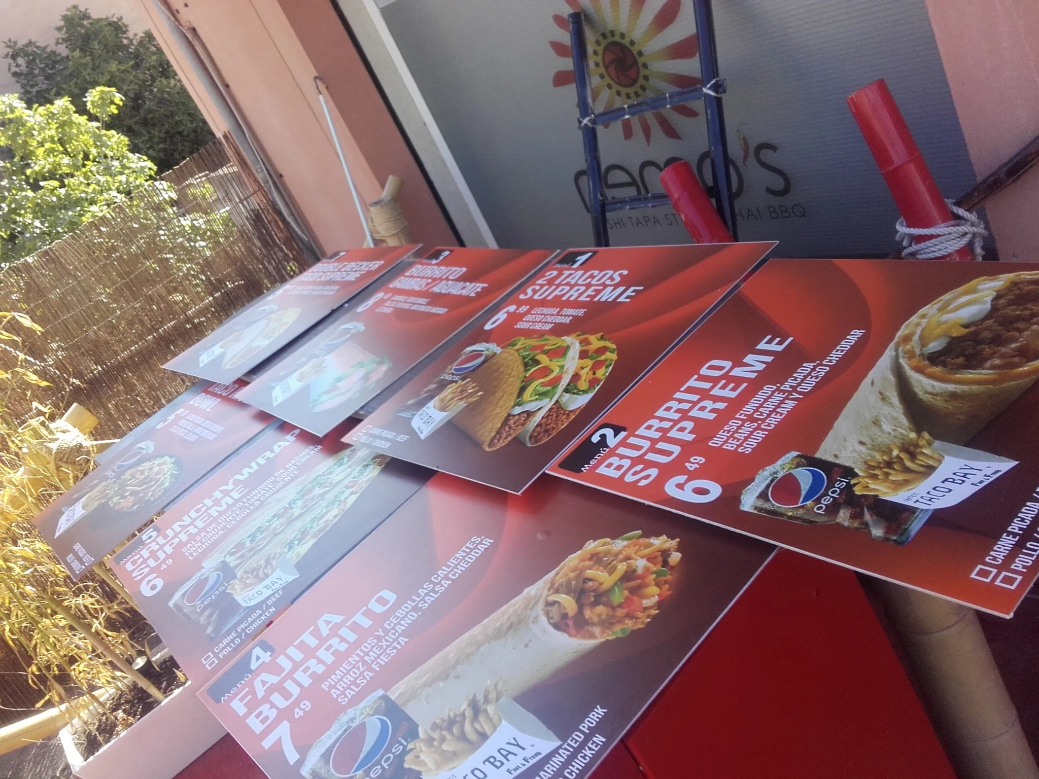 Menú de un restaurante que muestra diferentes tipos de tacos, con textos en español que describen las opciones y precios, en un entorno al aire libre.