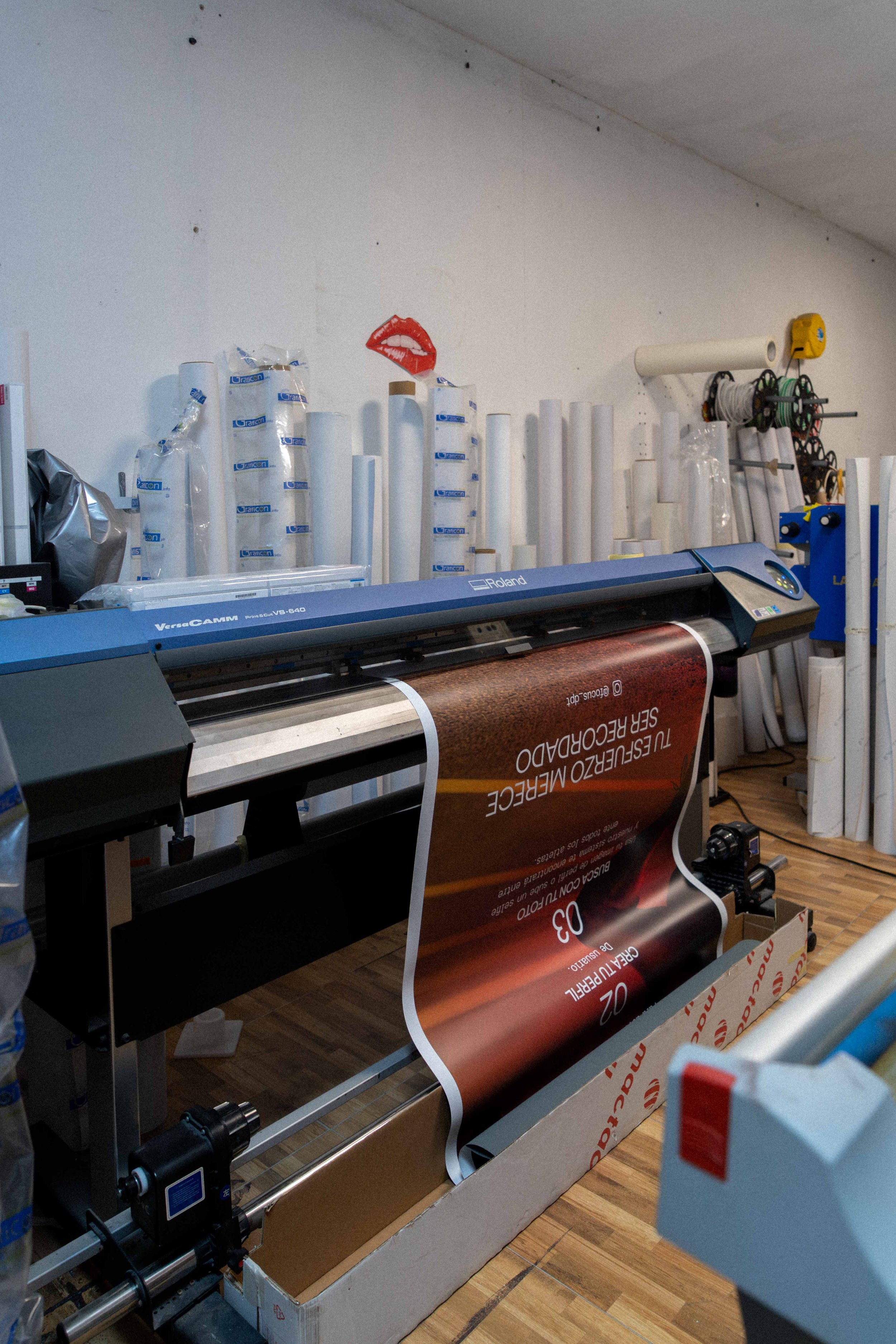 Rodillo de impresión digital con papel impreso en rollo en un taller de impresión, rodeado de tubos de papel y herramientas.
