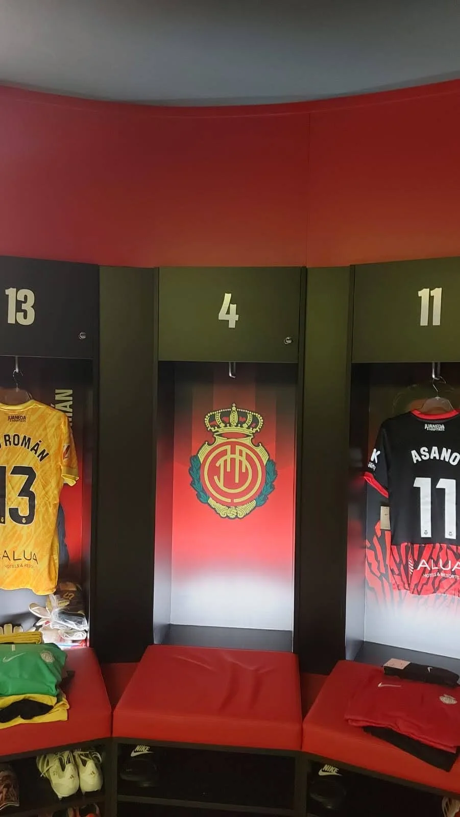 Vestidores con números 13, 4 y 11, con camisetas de fútbol colgadas y el escudo del club en la pared central.