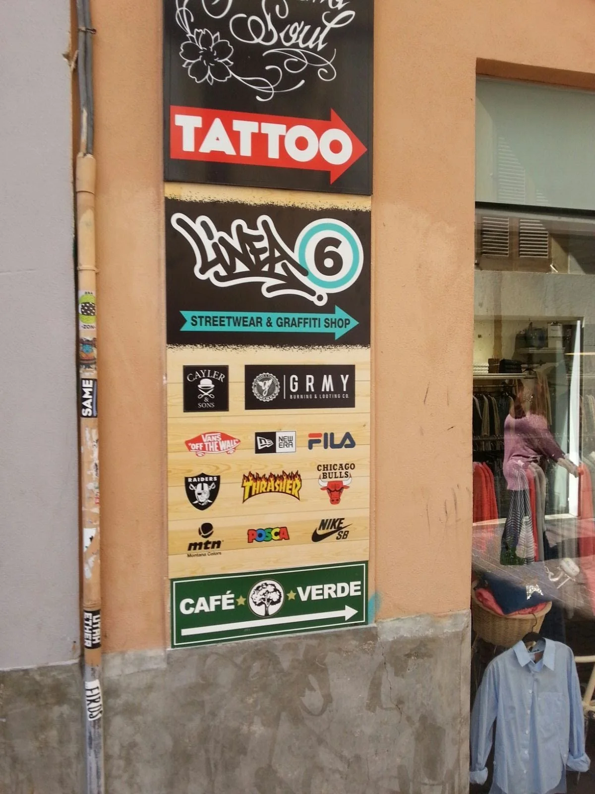 Señal de tienda con logos de diferentes marcas y anuncios, incluyendo un letrero verde que indica 'Café Verde' con una flecha apuntando hacia la derecha.