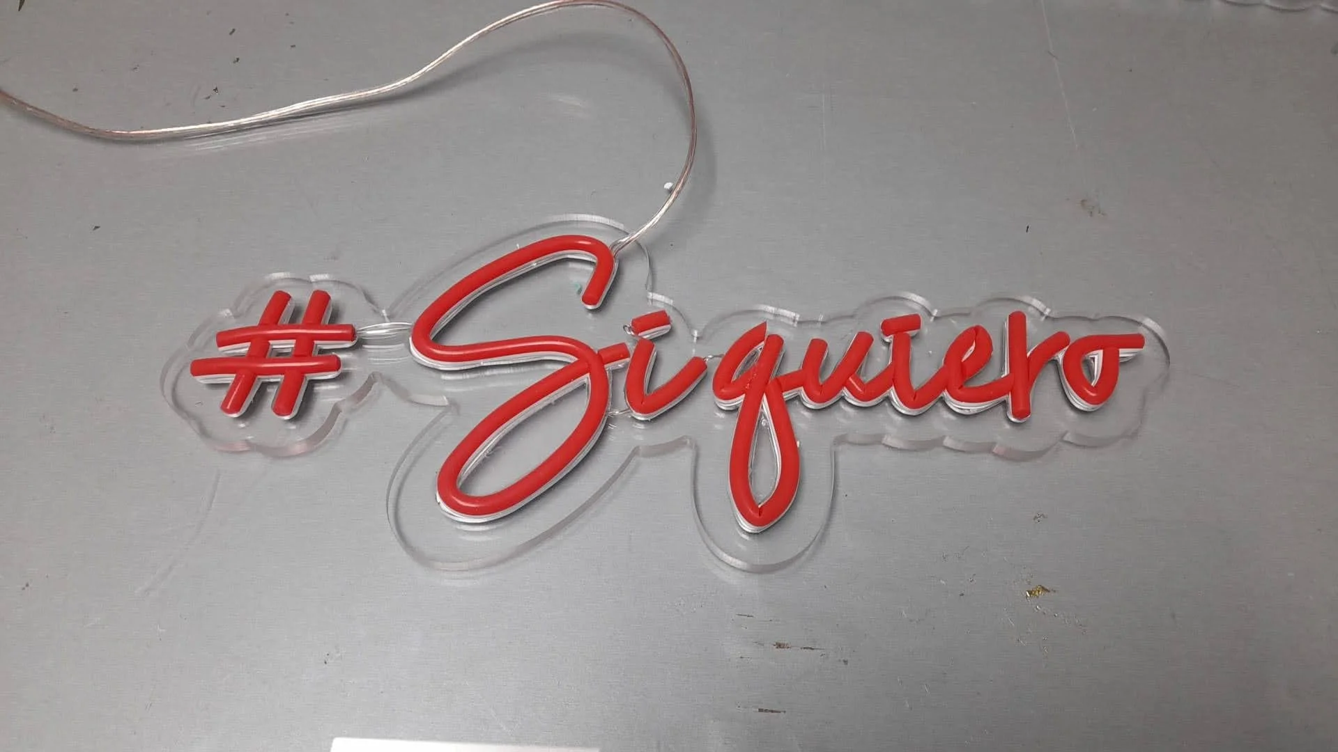 Signo de neón con el hashtag #SoyGuitero en letras rojas y un corazón en medio, colocado sobre una superficie gris.