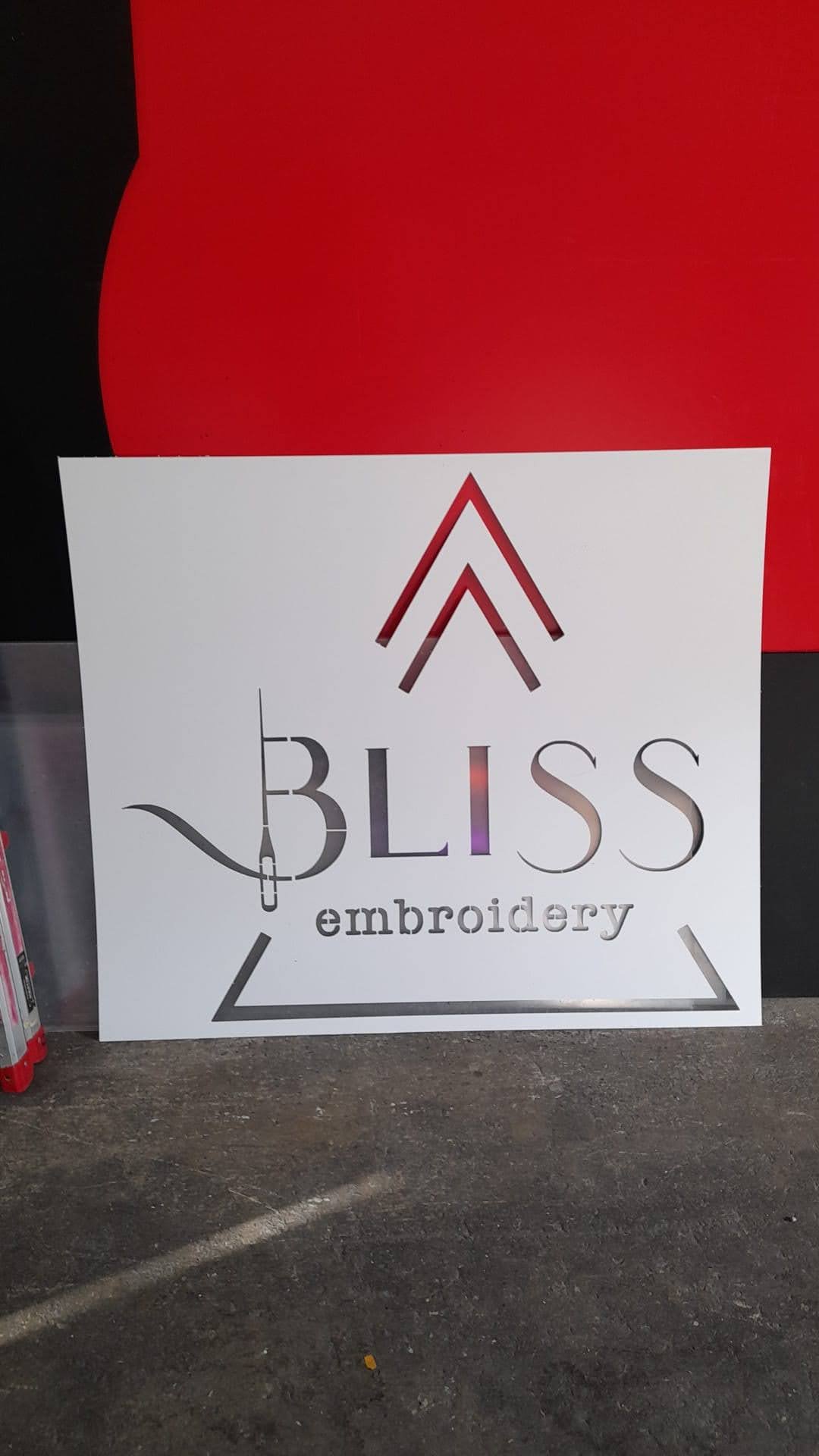 Cartel que dice 'Bliss Embroidery', con un diseño de flechas rojo y negro y un símbolo de aguja e hilo.