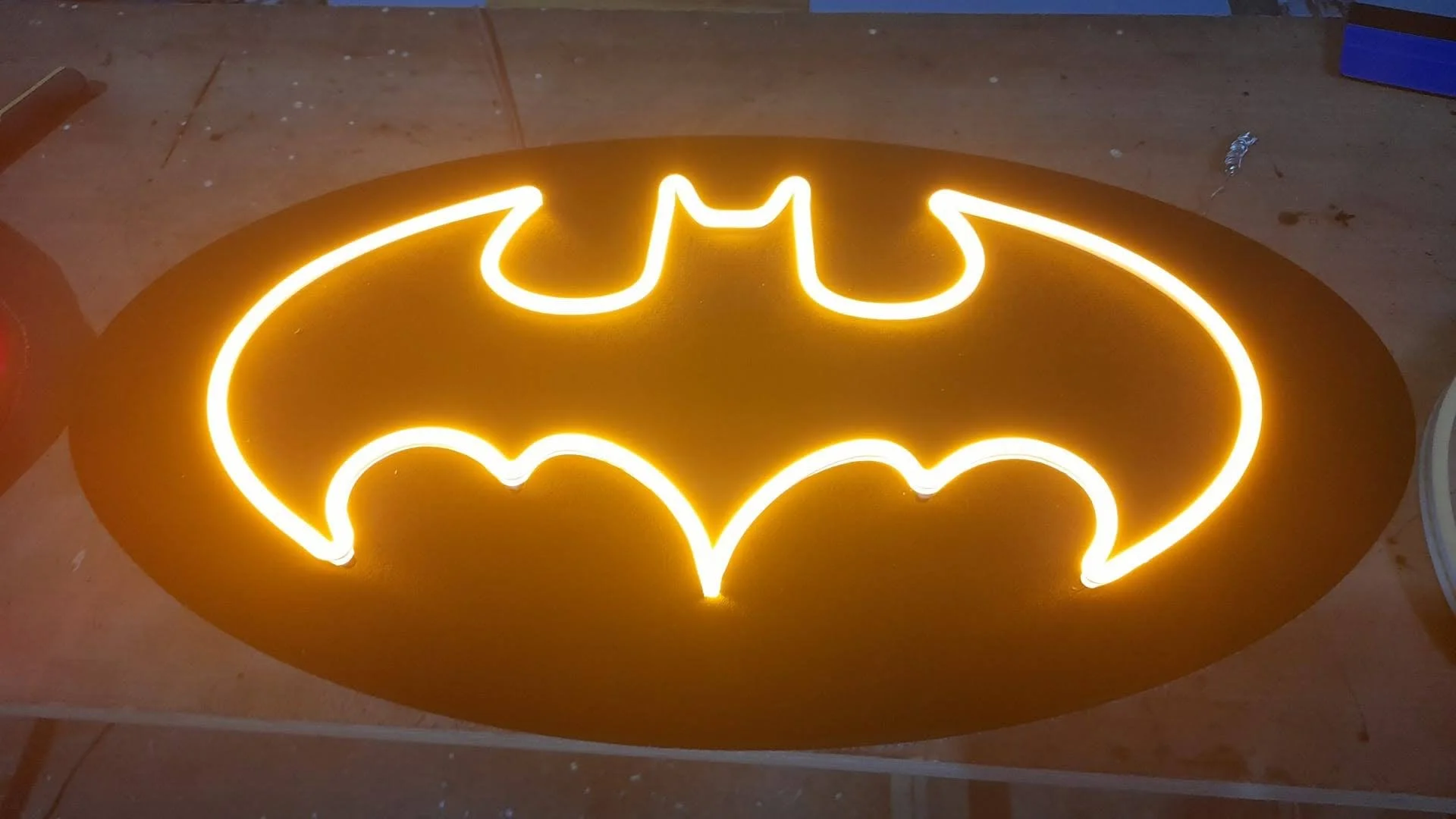 Letrero con el logo de Batman en neón amarillo sobre fondo negro.