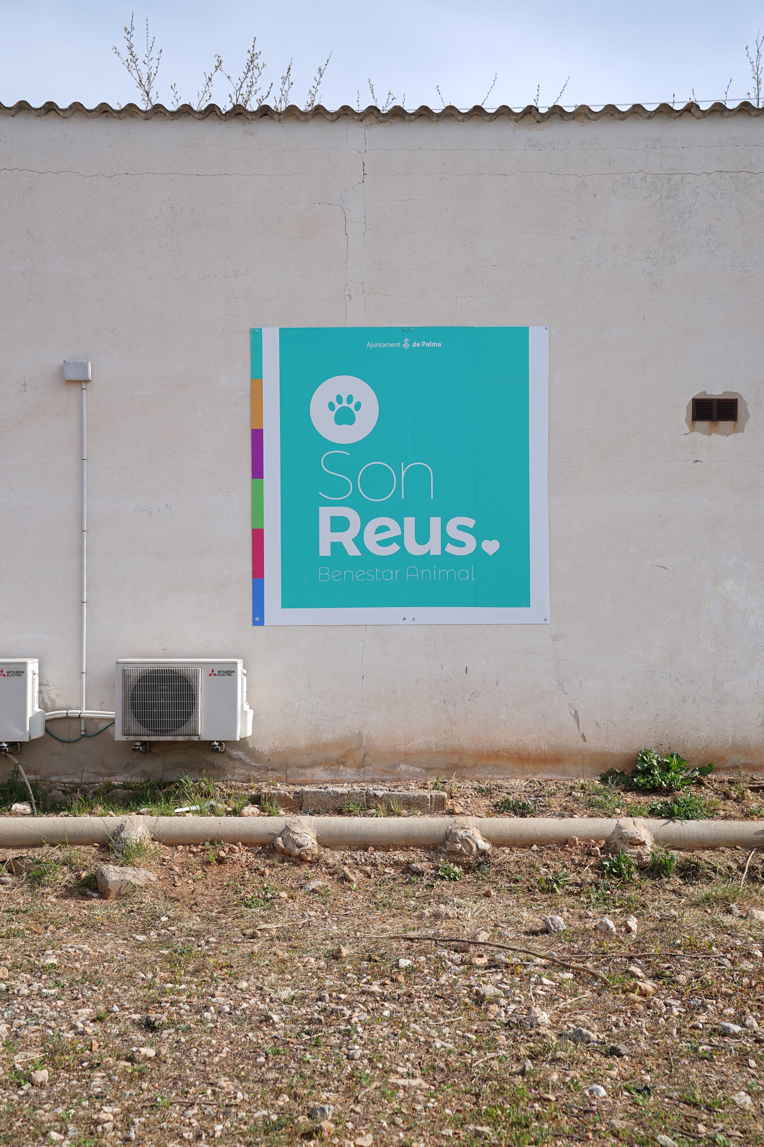 Cartel en la pared de un edificio que dice 'Son Reus. Benestar Animal' con un icono de pata de animal en un círculo blanco