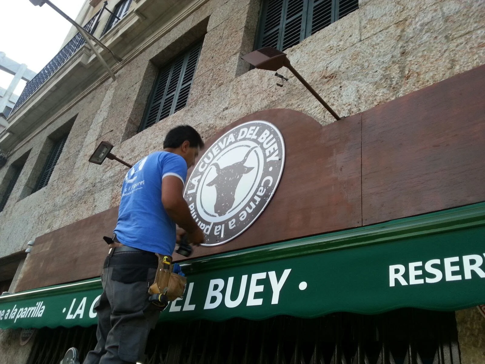 Un hombre colocando un logo en la fachada de un edificio que dice 'La Cueva del Buey'.
