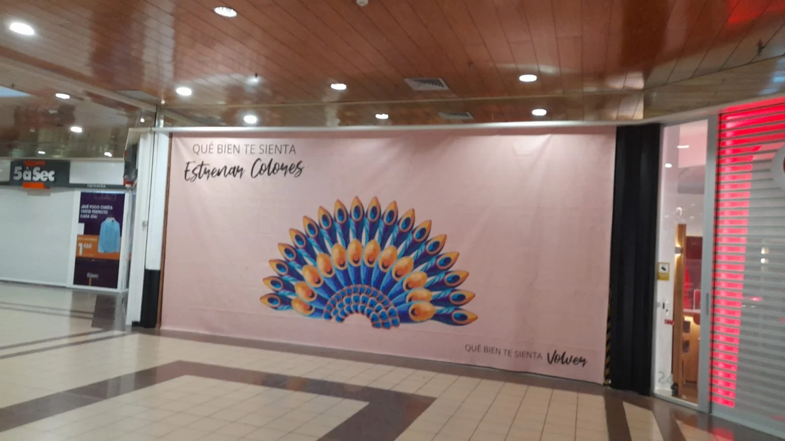 Cartel publicitario que muestra un peacock con sus plumas abiertas y el texto en español "Qué bien te sienta vestirnos. Que bien te sienta Volvex" en un establecimiento cerrado.
