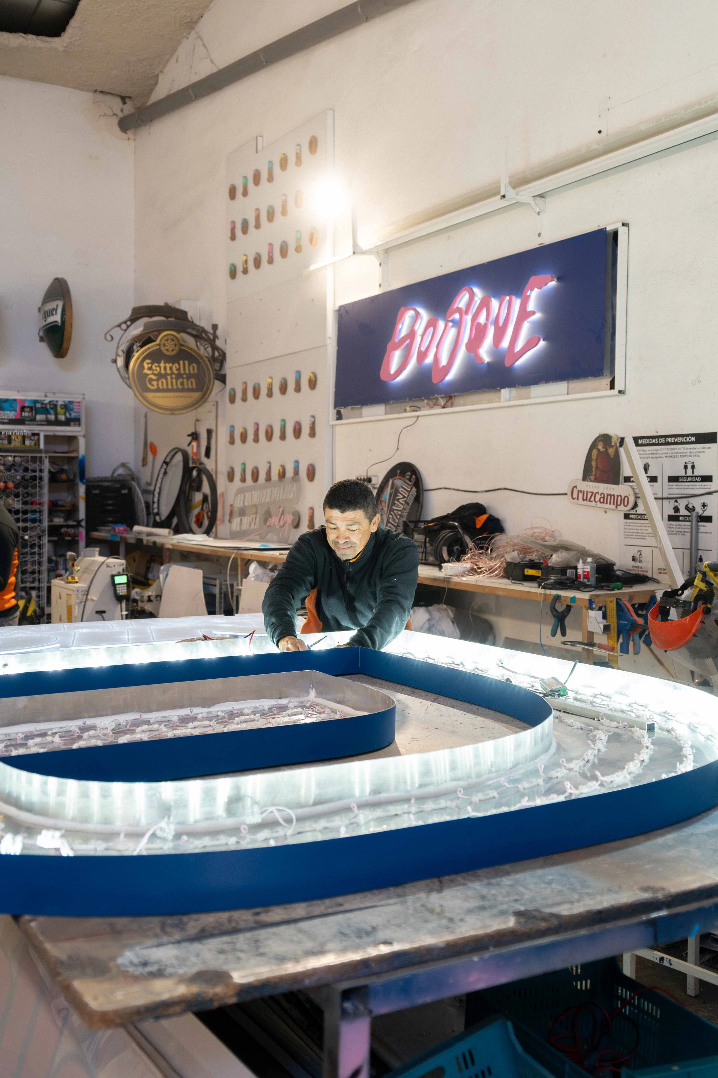 Un hombre trabajando en la fabricación de un letrero de neón que dice 'Barque' en un taller.