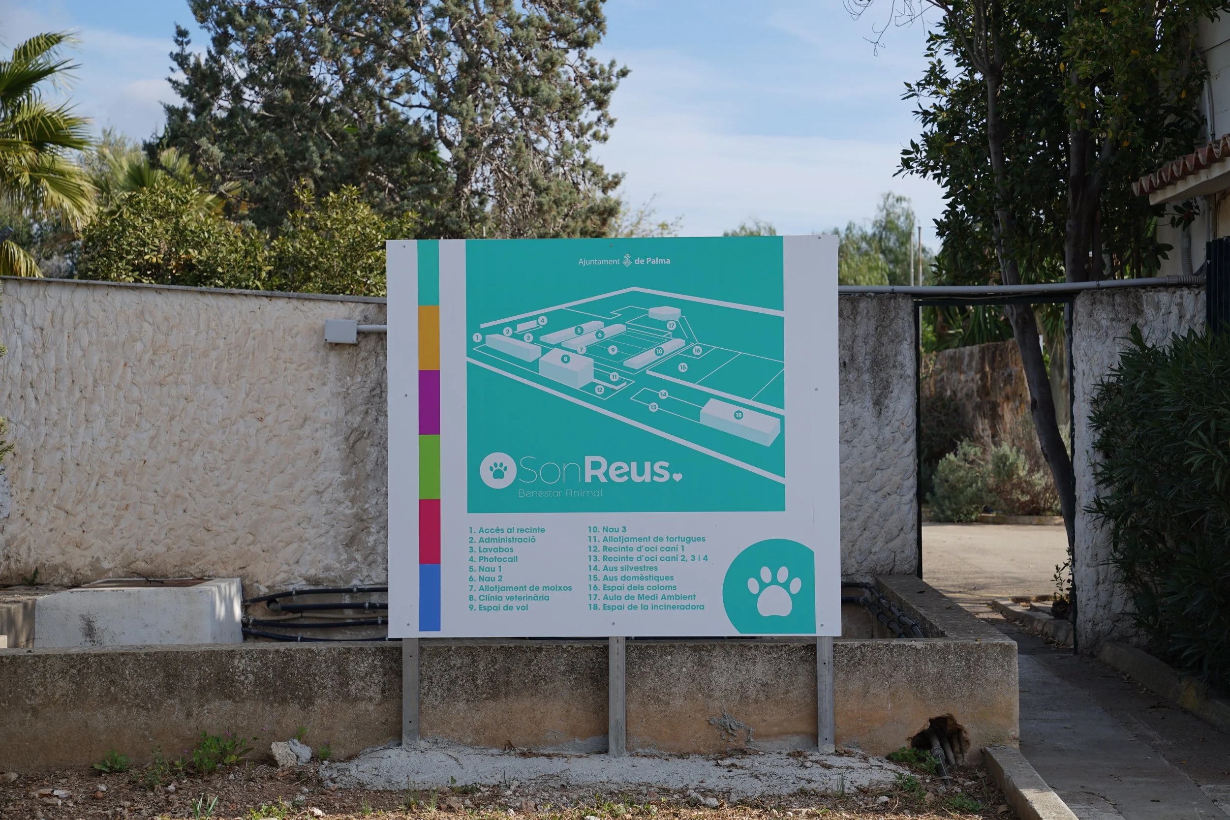 Cartel informativo con un mapa del zoológico SonReus en Palma, con áreas y paseos de animales, refugios y espacios recreativos, en un entorno exterior con paredes de piedra y árboles.