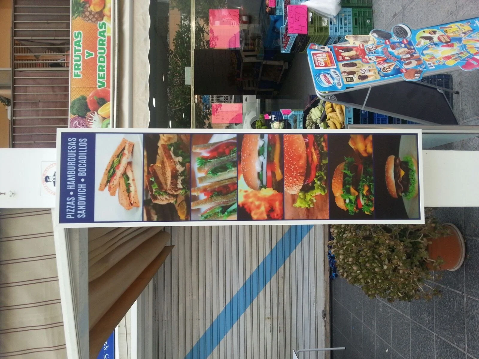 Cartel de comida rápida con fotos de diferentes tipos de hamburguesas y sándwiches, con texto en español que dice 'Pizzas, Hamburguesas, Sandwich, Bocadillos'.