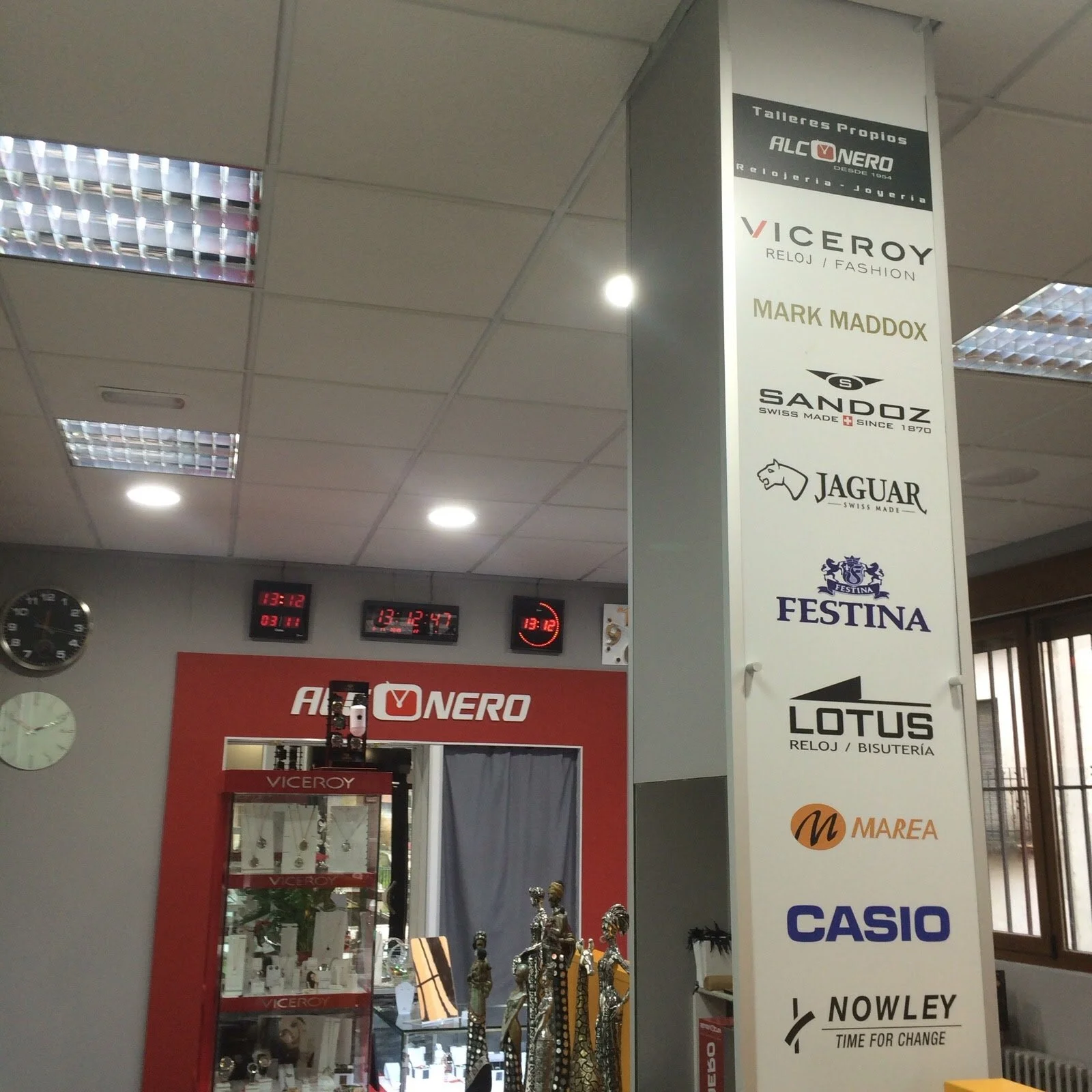 Cartel promocional de varias marcas de relojes, joyería y bisutería, incluido Viceroy, Sandoz, Jaguar, Festina, Lotus y Casio, en un establecimiento comercial.