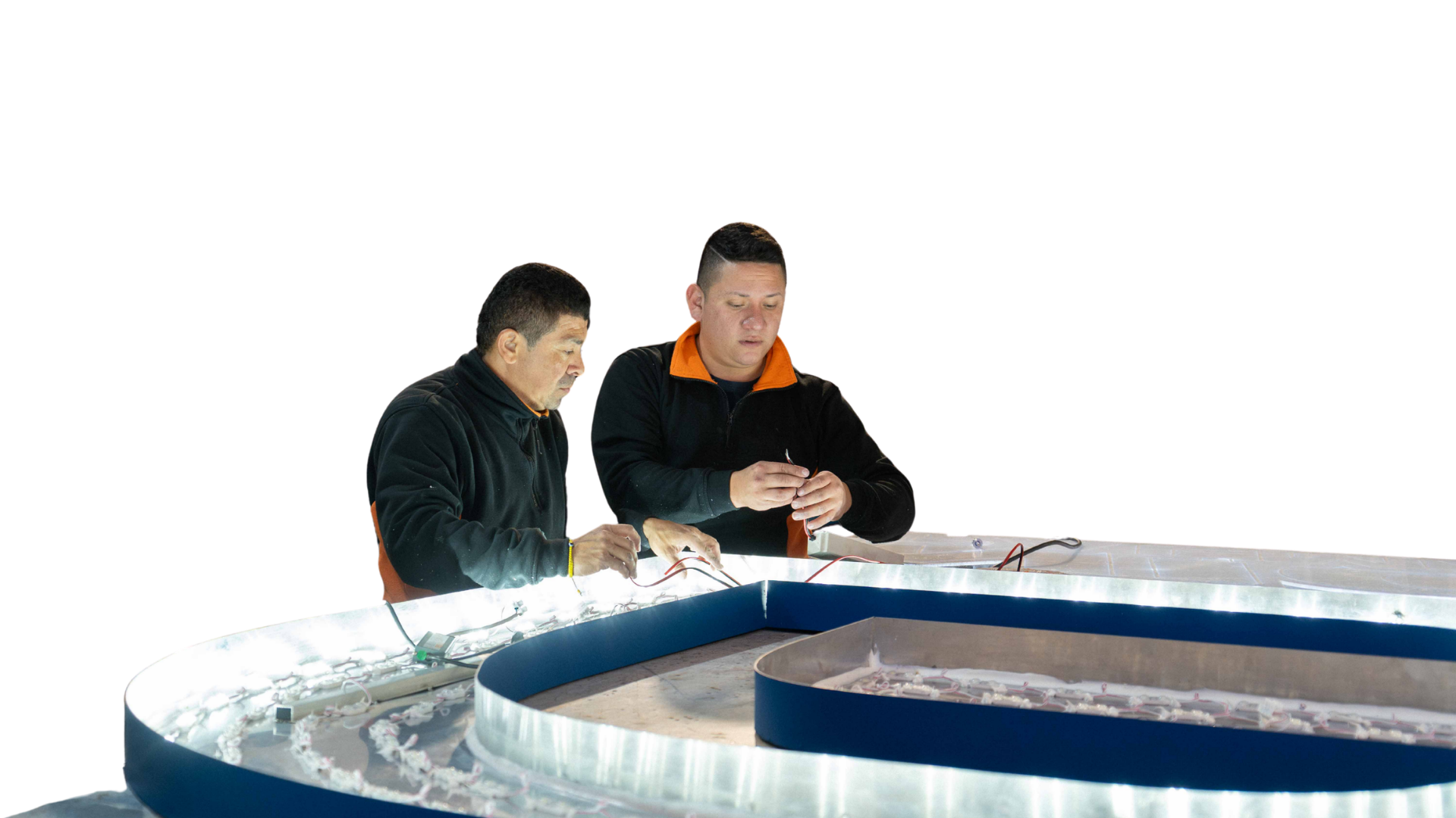 Dos jóvenes construyen y conectan componentes electrónicos en una mesa de trabajo, con un fondo negro.