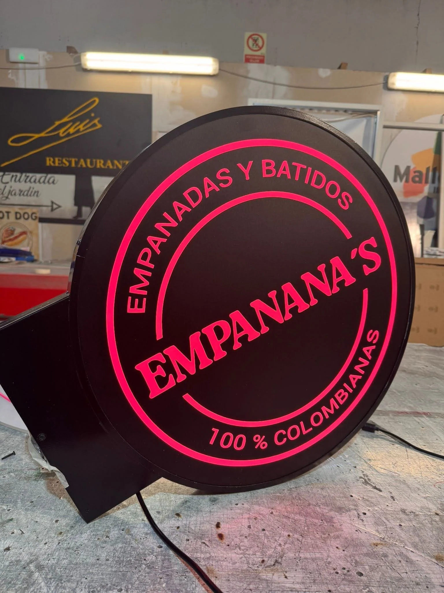 Rótulo luminoso que dice 'Empanadas y Batidos', con letras en color rosa y fondo negro, y menciona '100% colombianas'.