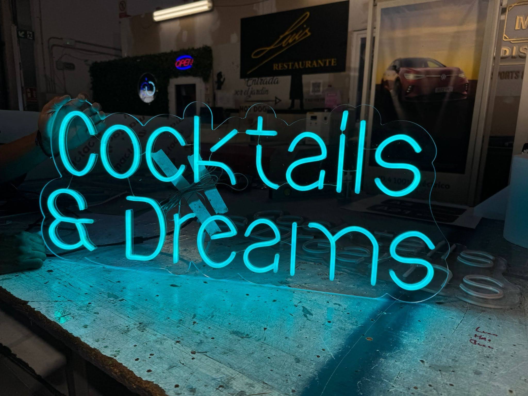 Letrero de neón en color azul que dice 'COCINA' en un fondo oscuro, reflejado en una superficie de cristal.