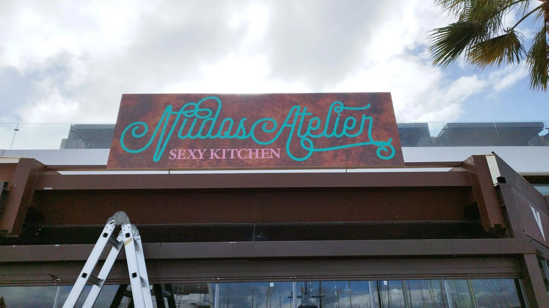 Cartel del negocio 'Múdas Atelier' con la frase 'Sexy Kitchen' en la parte inferior.