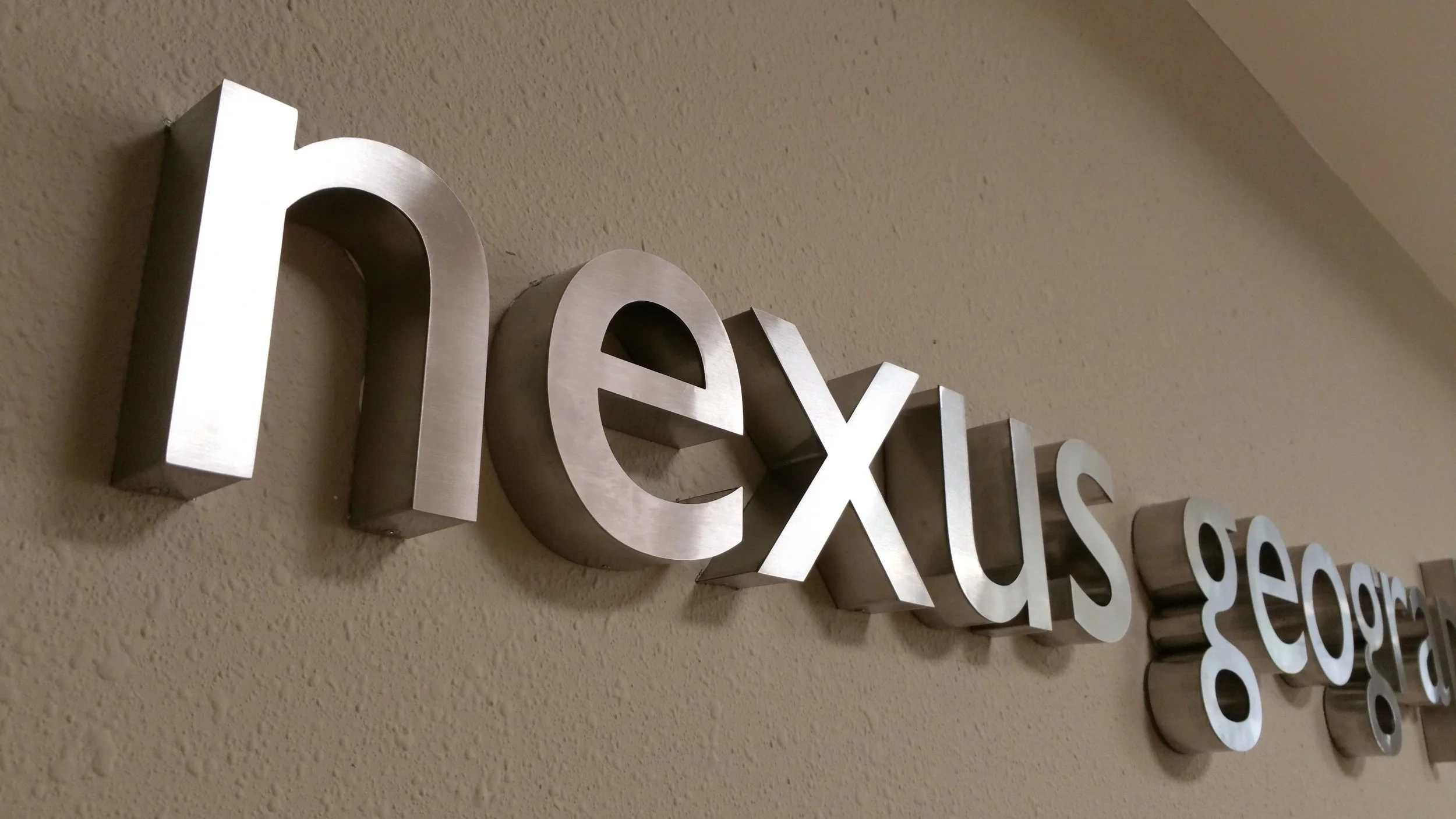 Letra metálica en la pared que dice 'next' en letras mayúsculas y en relieve.