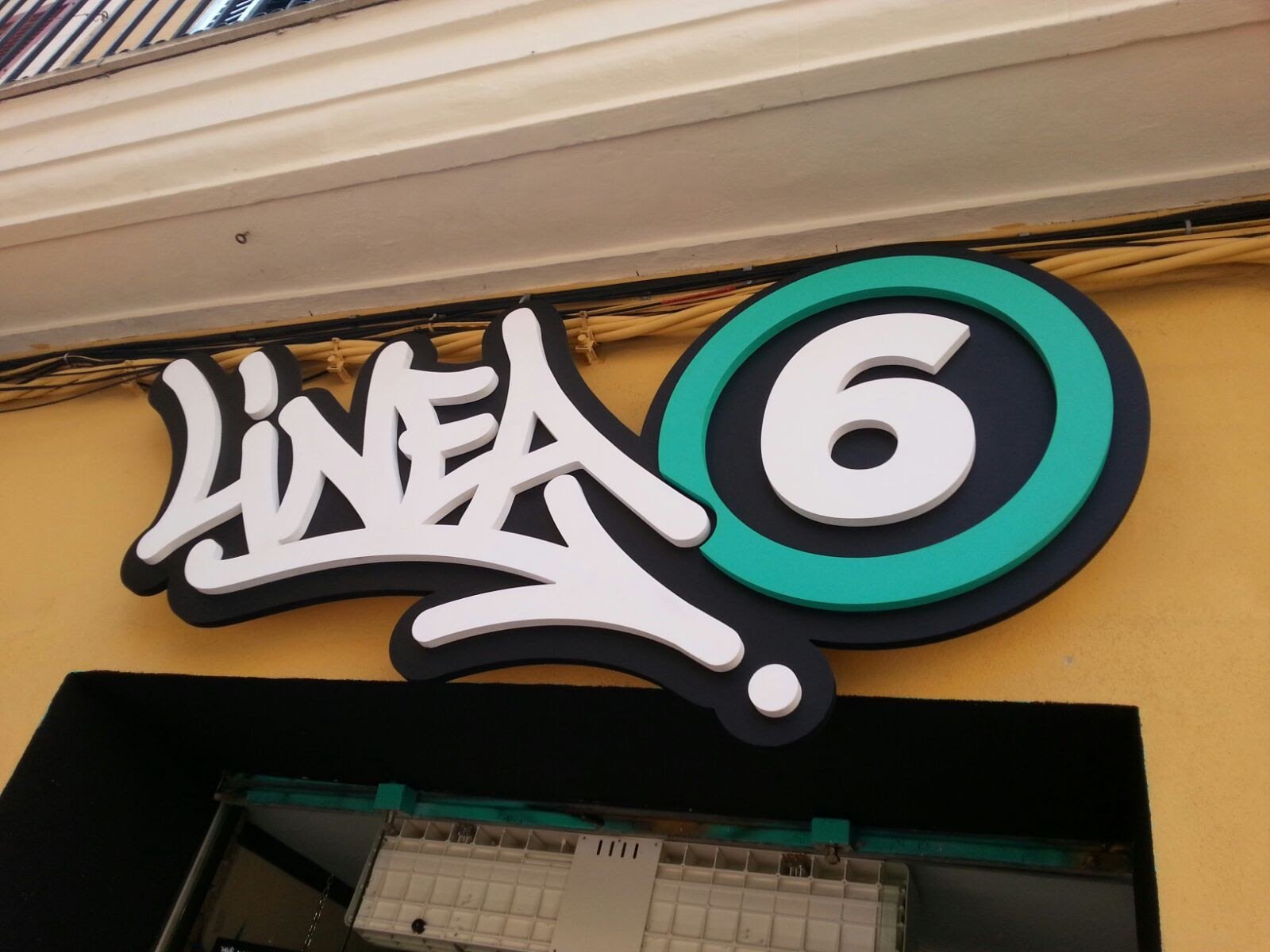 Cartel de la tienda 'Línea 6' en un edificio de color amarillo con moldura blanca en la parte superior.