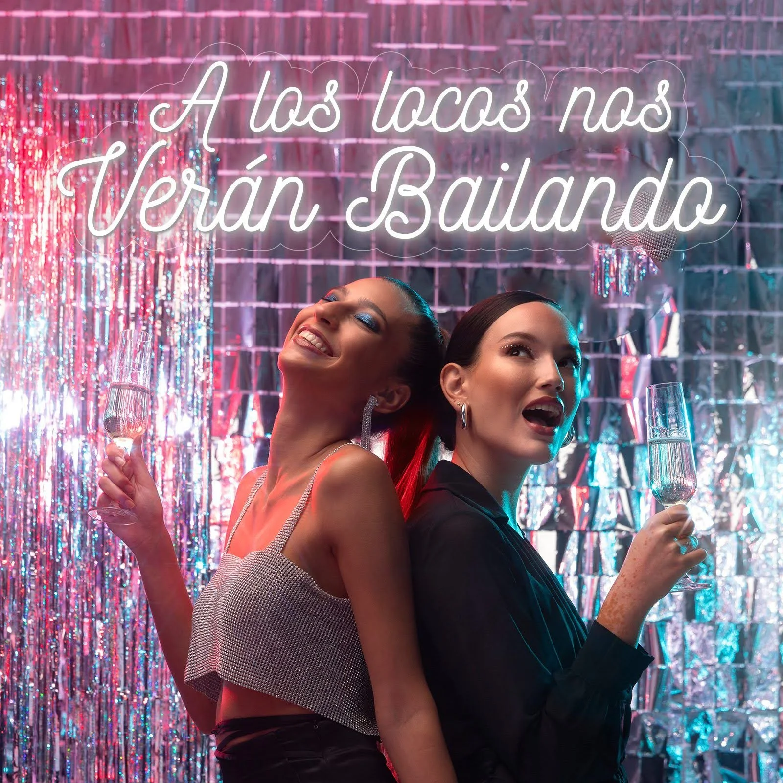 Dos mujeres con luces de maquillaje y peinados llamativos, brindando con copas de champán en una fiesta con fondo de decoraciones brillantes y coloridas.