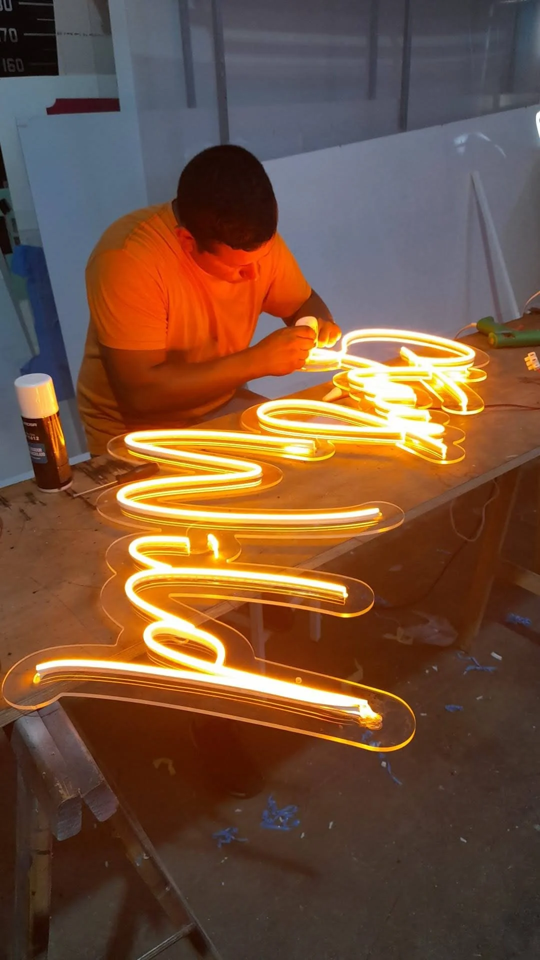 Persona trabajando con neón de color naranja brillante en un taller, creando letras o signos luminosos.