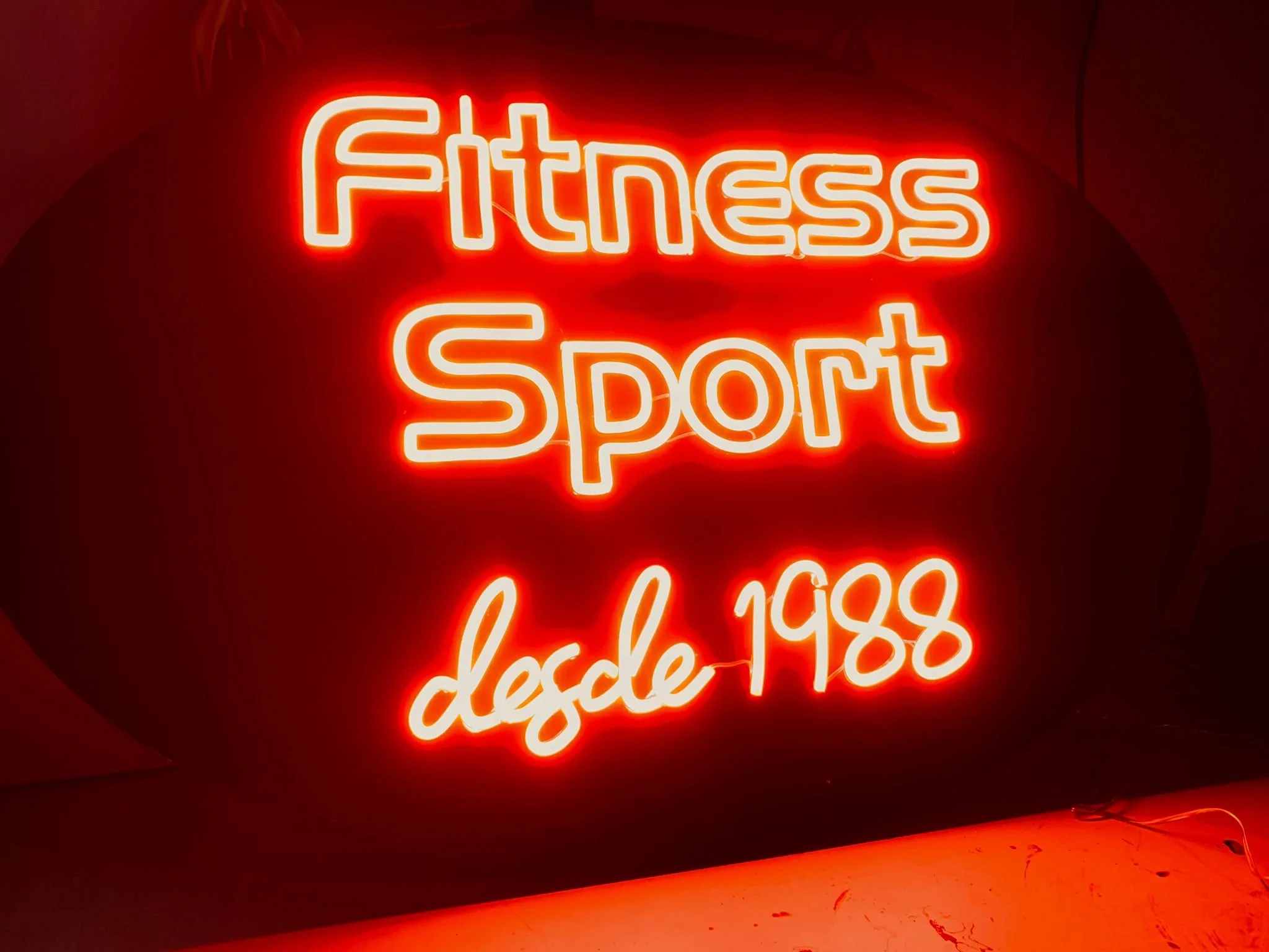 Cartel de neón en color rojo que dice 'Fitness Sport', iluminando el fondo oscuro.
