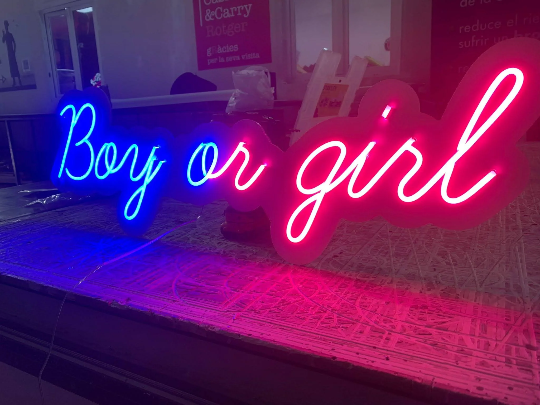 Un letrero luminoso en colores azules y rosados que dice 'boy you got' en un establecimiento con paredes rosas y una mesa de madera.