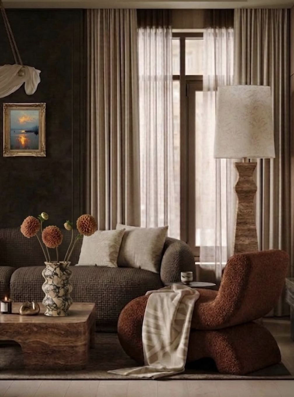 Living room with brown patterned sofa, beige pillows, tall marble lamp, sheer curtains, art painting, decorative vase with orange flowers, armchair with a draped beige and white striped fabric.