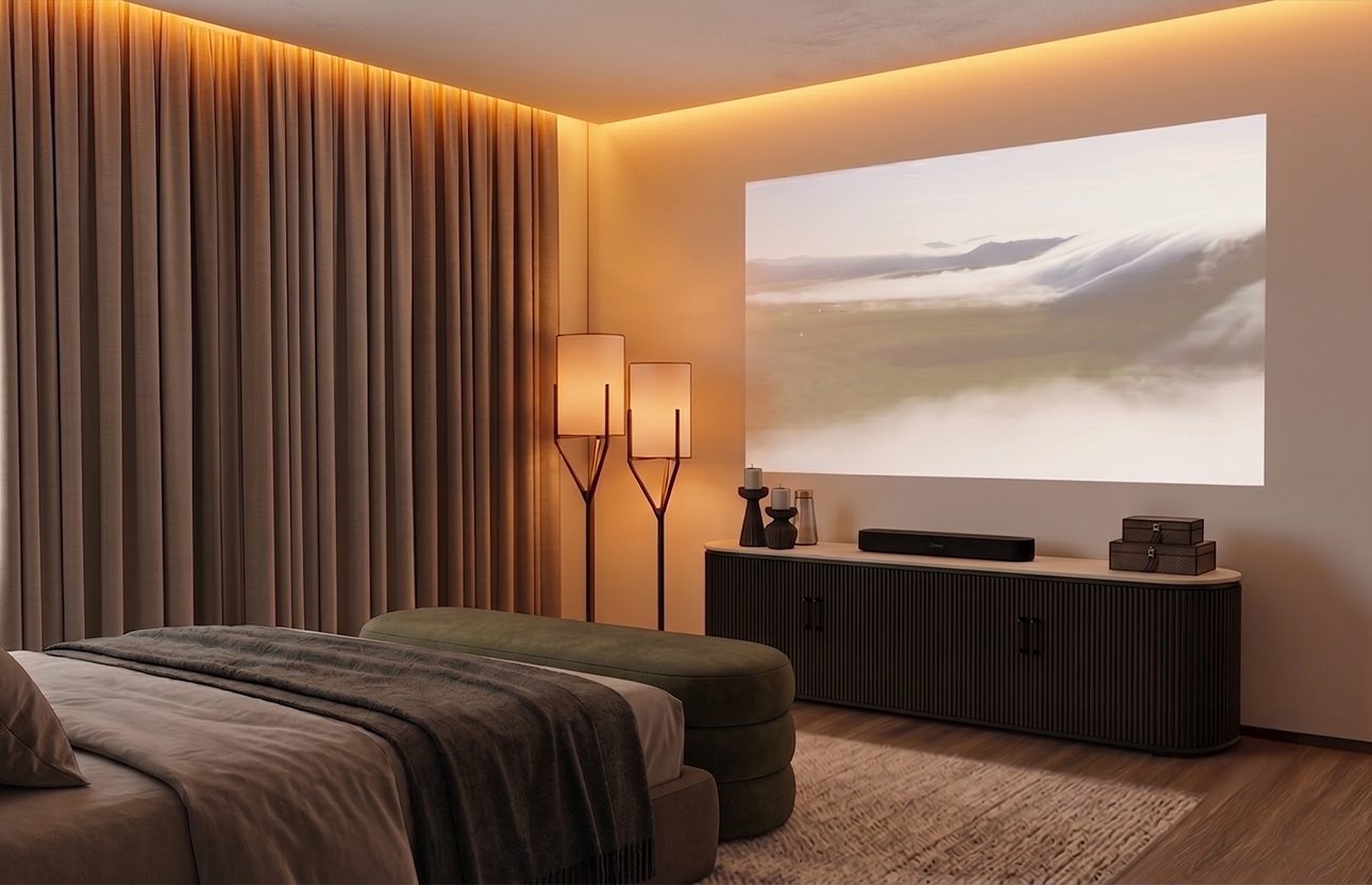A bedroom with beige curtains, a bed with neutral bedding and a dark throw, a green ottoman at the foot of the bed, a beige rug, a black media console, a large wall projection of a landscape, and a pair of tall modern floor lamps with white shades.