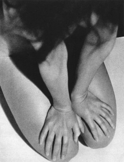 A person lying on their back with their knees bent, hands on their knees, and head turned to the side, in black and white photo.
