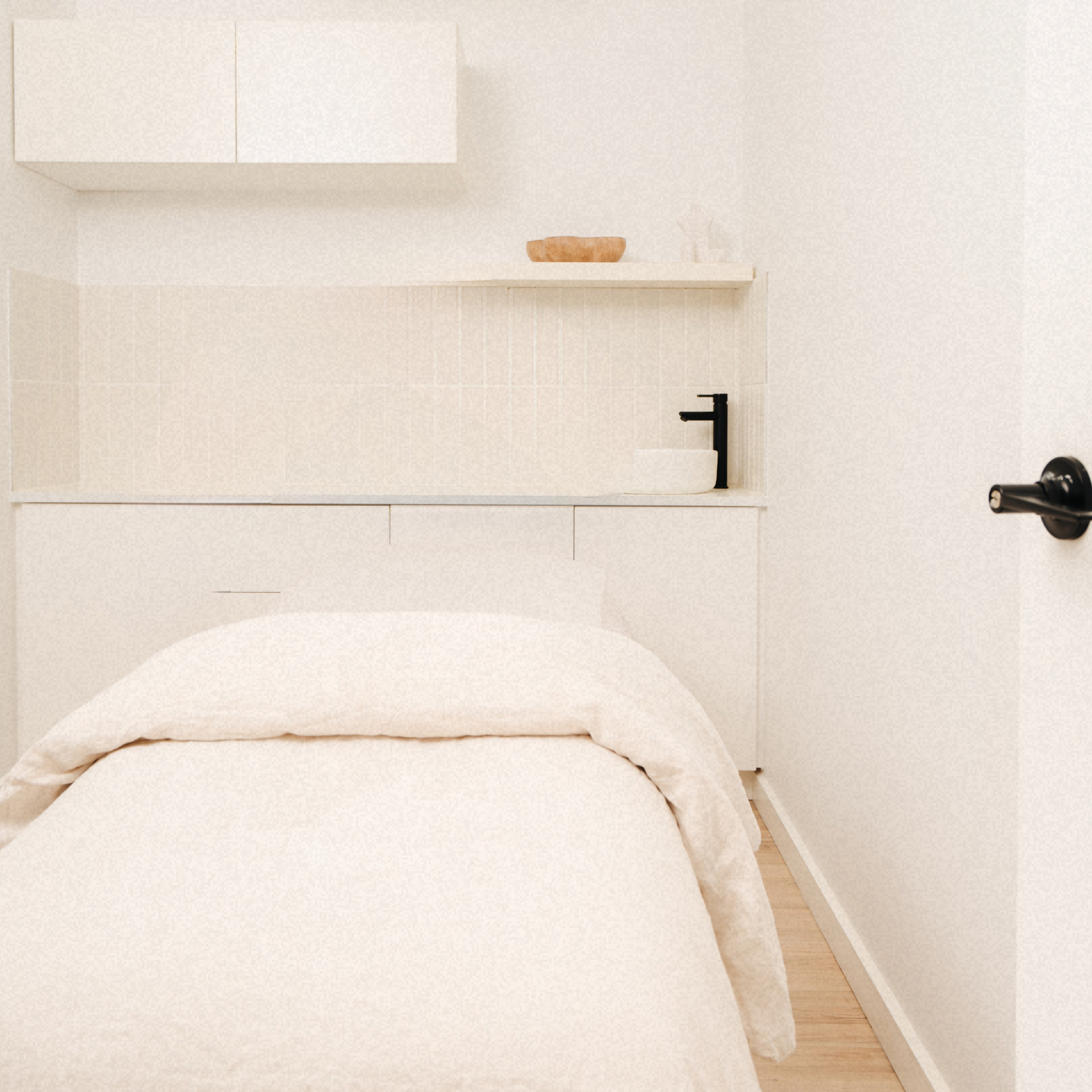 Minimalistic bedroom with a beige bed, black faucet, and a small white sink in a white-themed room.