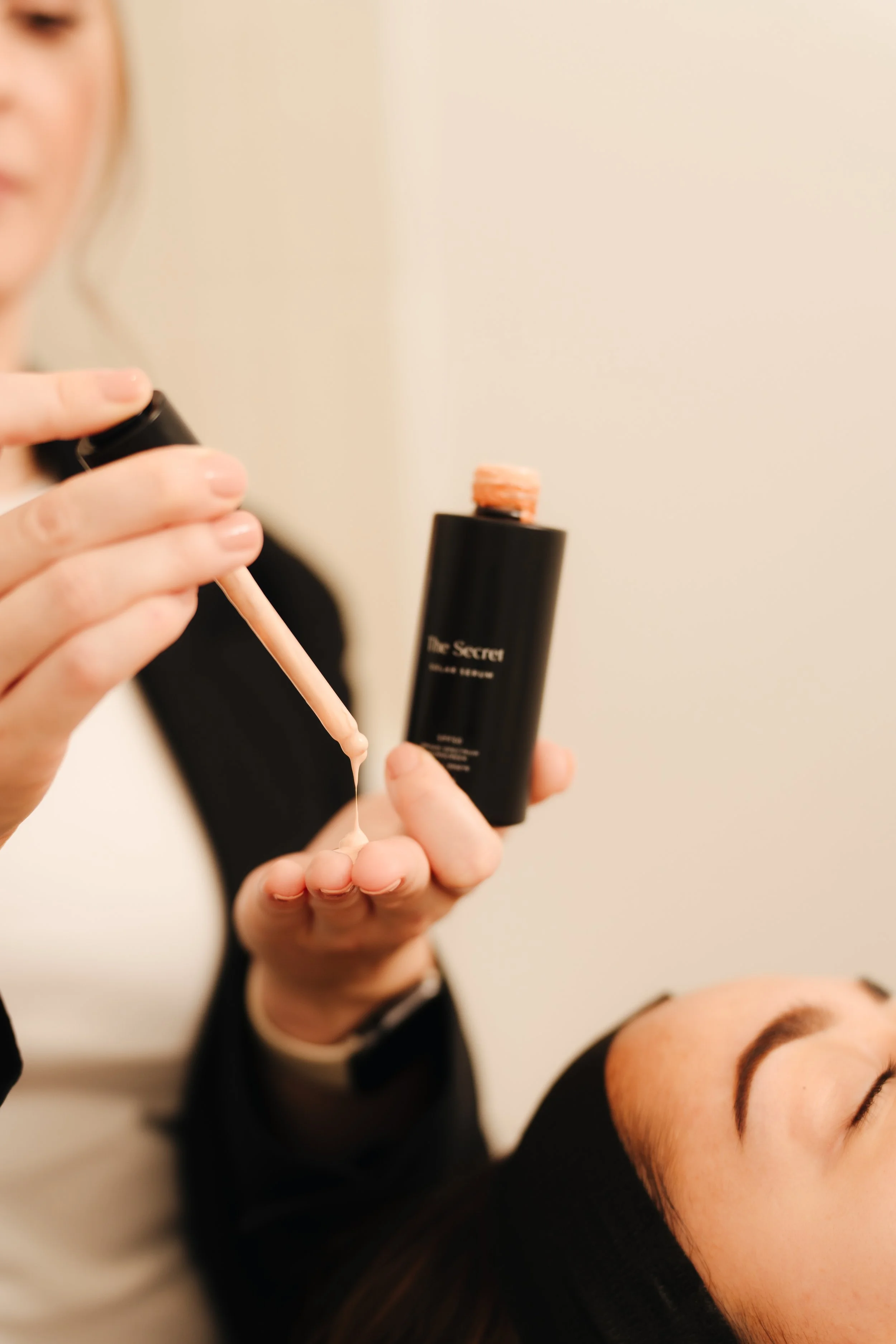 A woman applying a liquid makeup product using a dropper onto another woman's face during a beauty treatment.