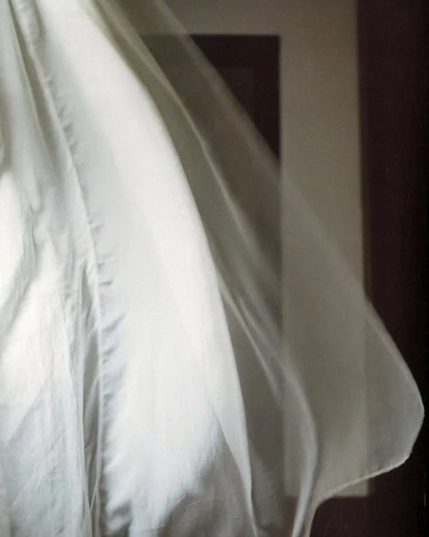 Close-up of a white satin dress or fabric on a hanger, with a dark background.