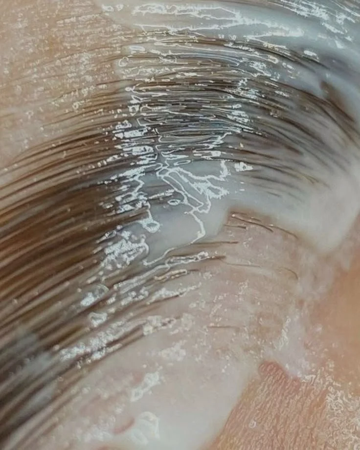 Close-up of a person's eyebrow, with a white cream or gel applied along the hairline, possibly for cosmetic or skincare purposes.