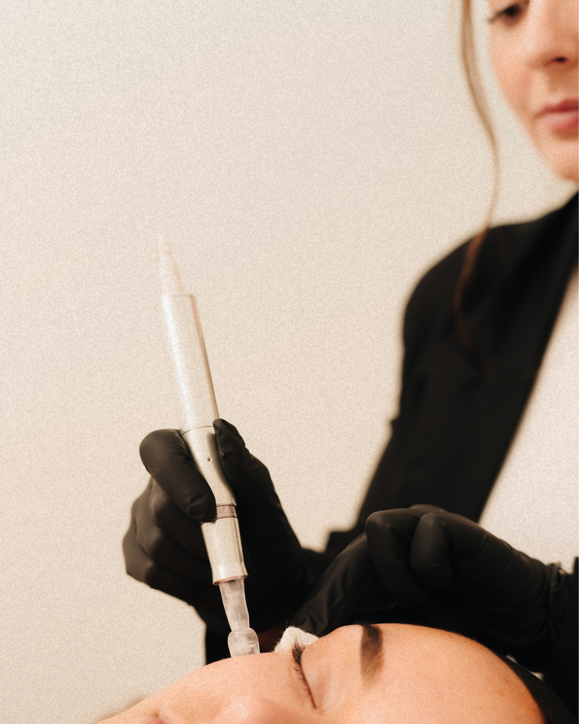 A woman in black gloves administering a cosmetic injection to a client’s forehead.