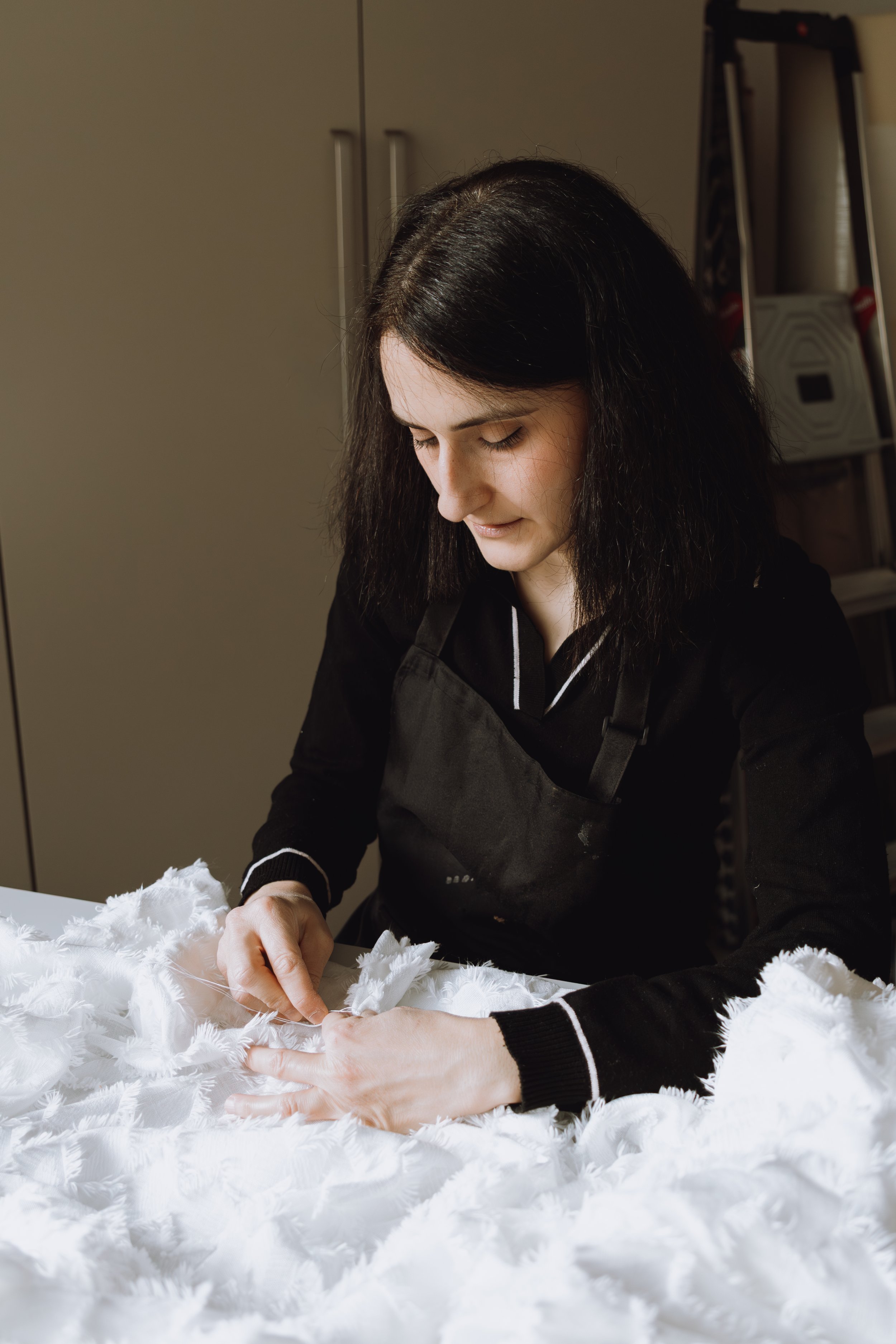 Femme aux cheveux noirs travaillant avec des plumes blanches sur une table