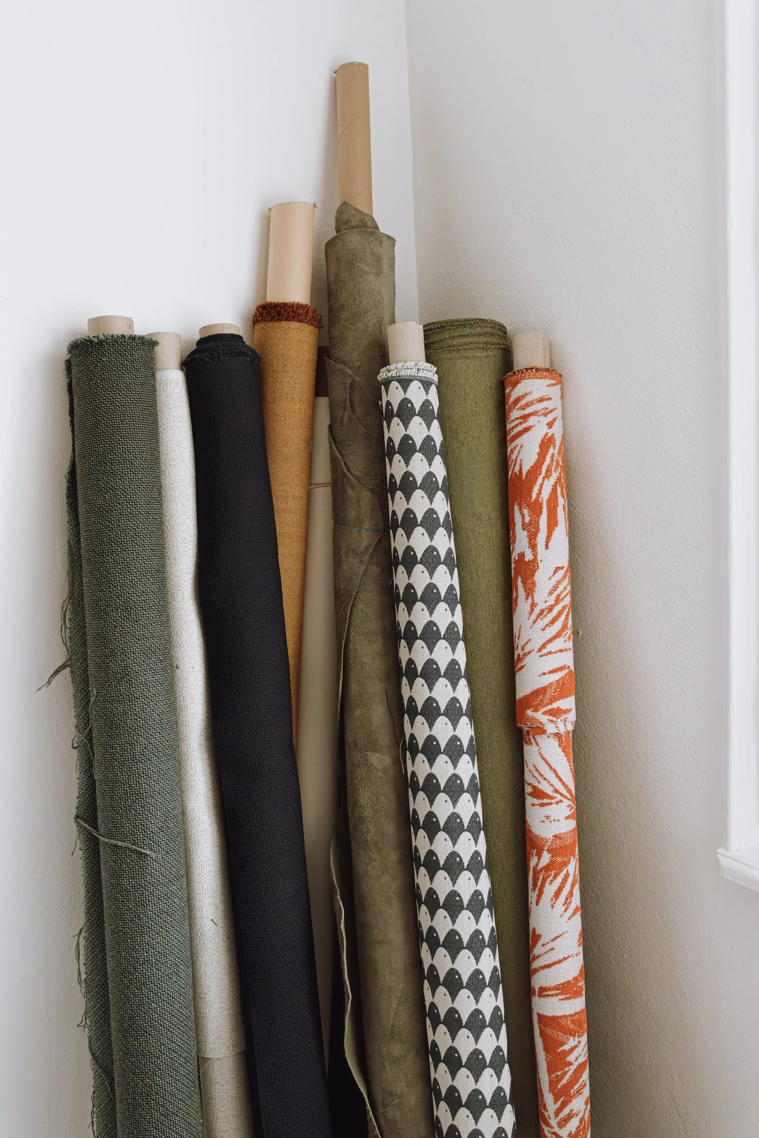 Rouleaux de tapis avec différentes couleurs et motifs, empilés contre un mur blanc.
